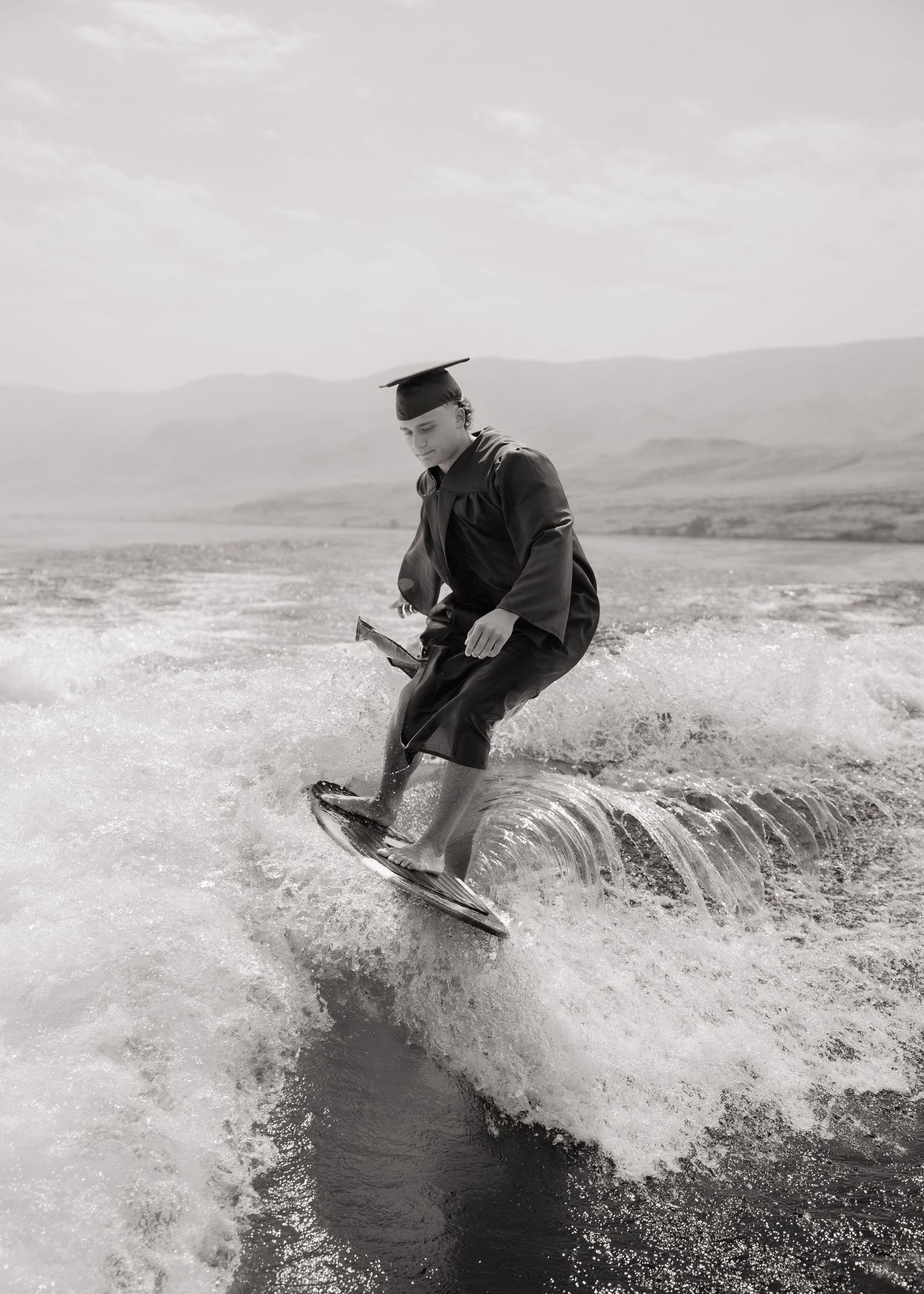 High school graduate wakesurfing in his cap and gown during an adventurous Washington senior portrait session.