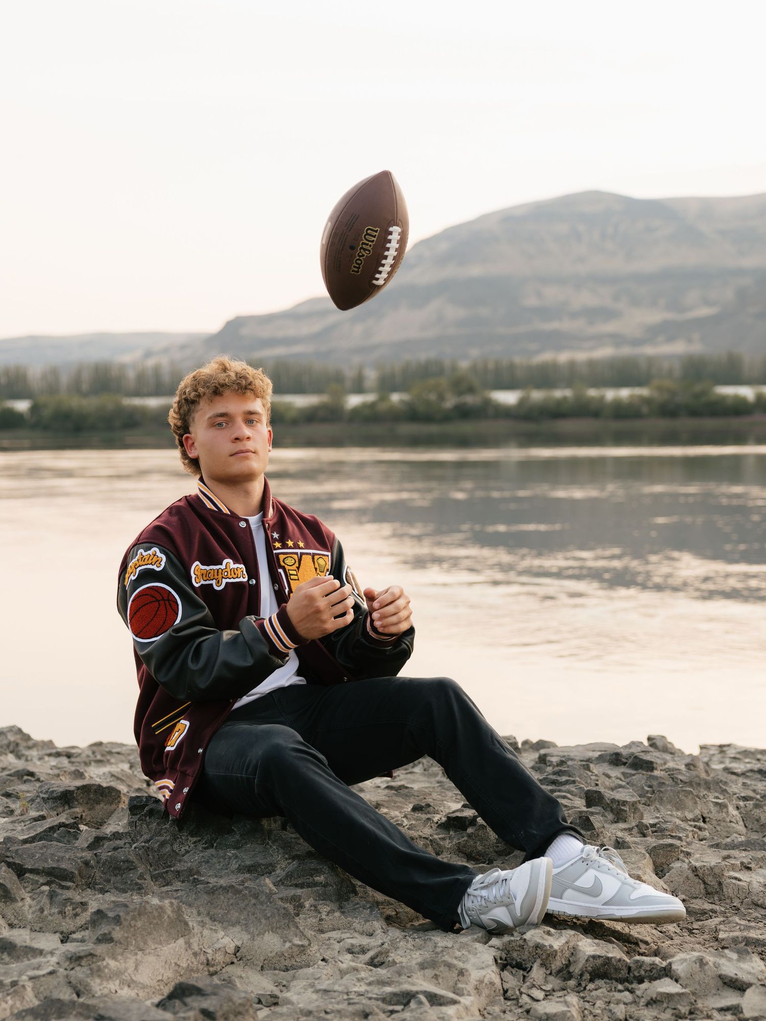 High school senior tossing a football by the water during an outdoor Washington senior photography session.
