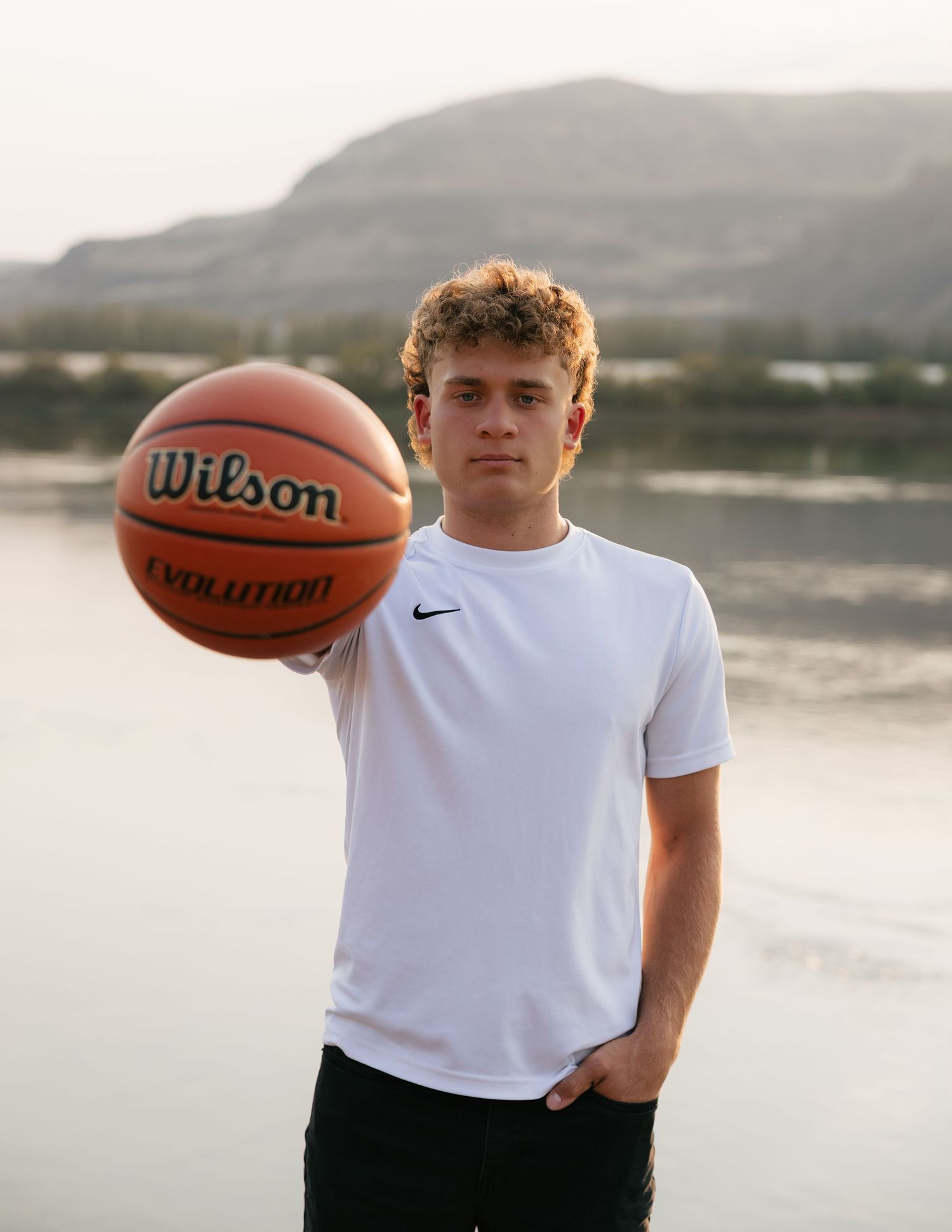 High school senior holding a basketball during an outdoor senior photography session by the water in Washington.