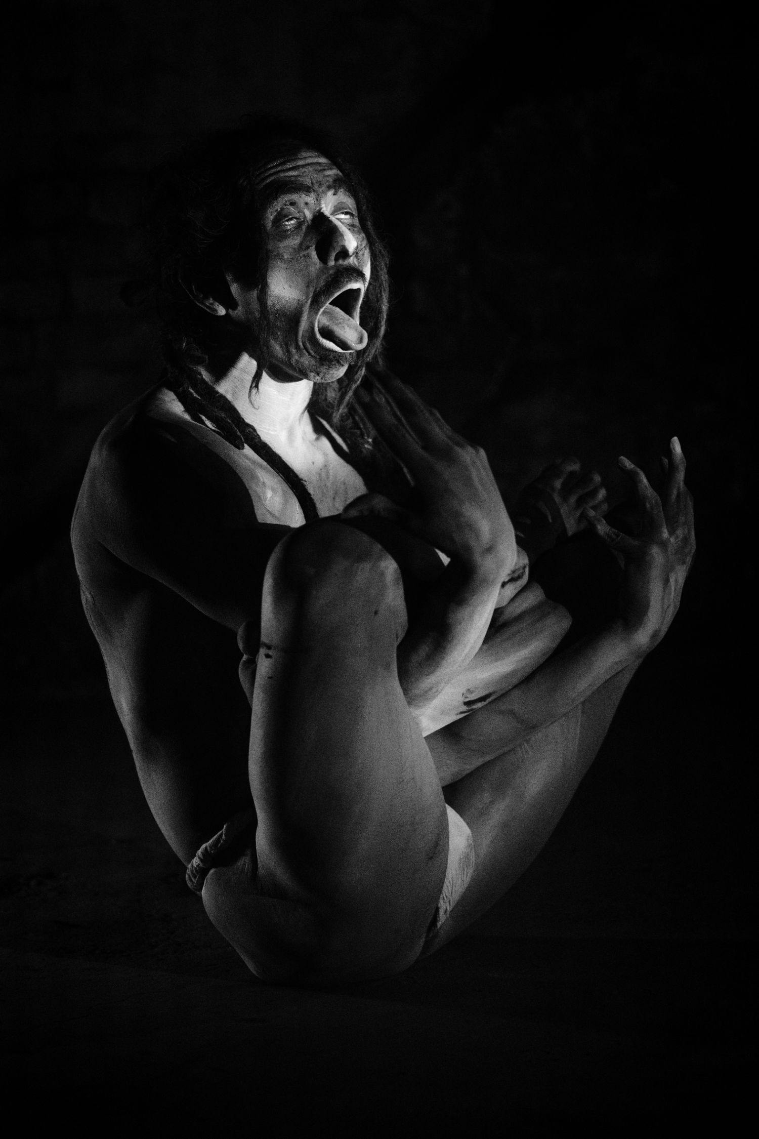 Black and white photo of a person in dramatic pose with open mouth expression against dark background.