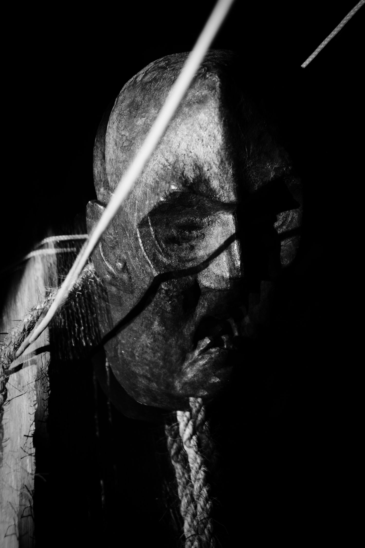 Dark black and white close-up of an aged, weathered sculpture face with dramatic shadows and diagonal lines.