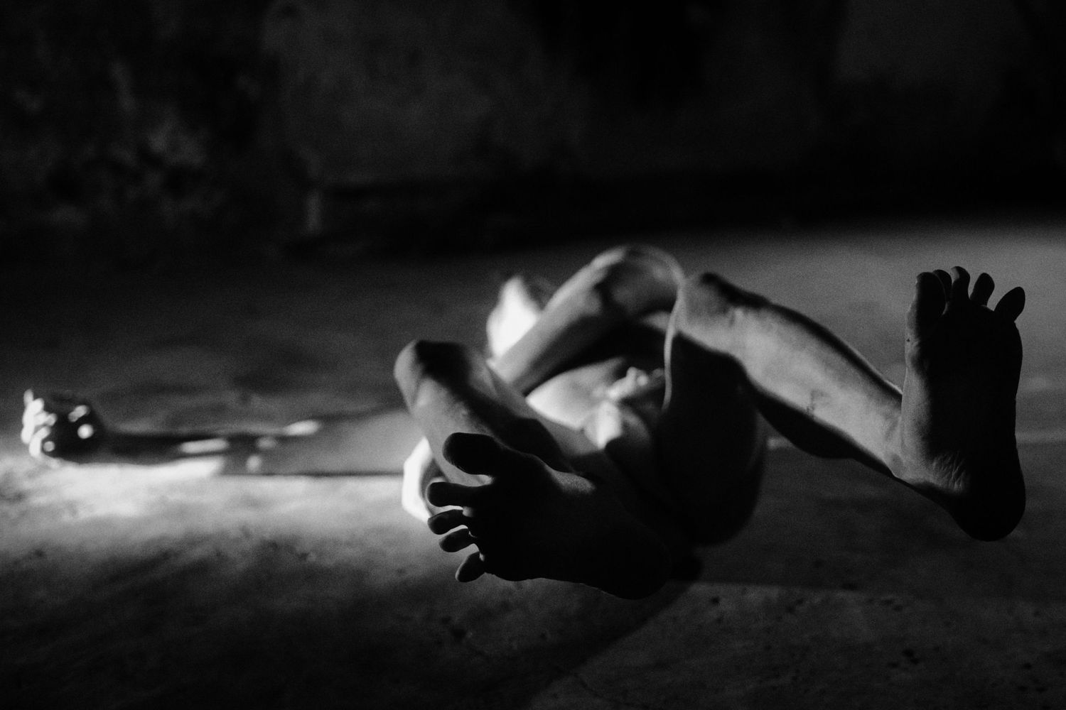 Black and white photo of a person lying on the ground in a dimly lit room, captured in artistic pose.