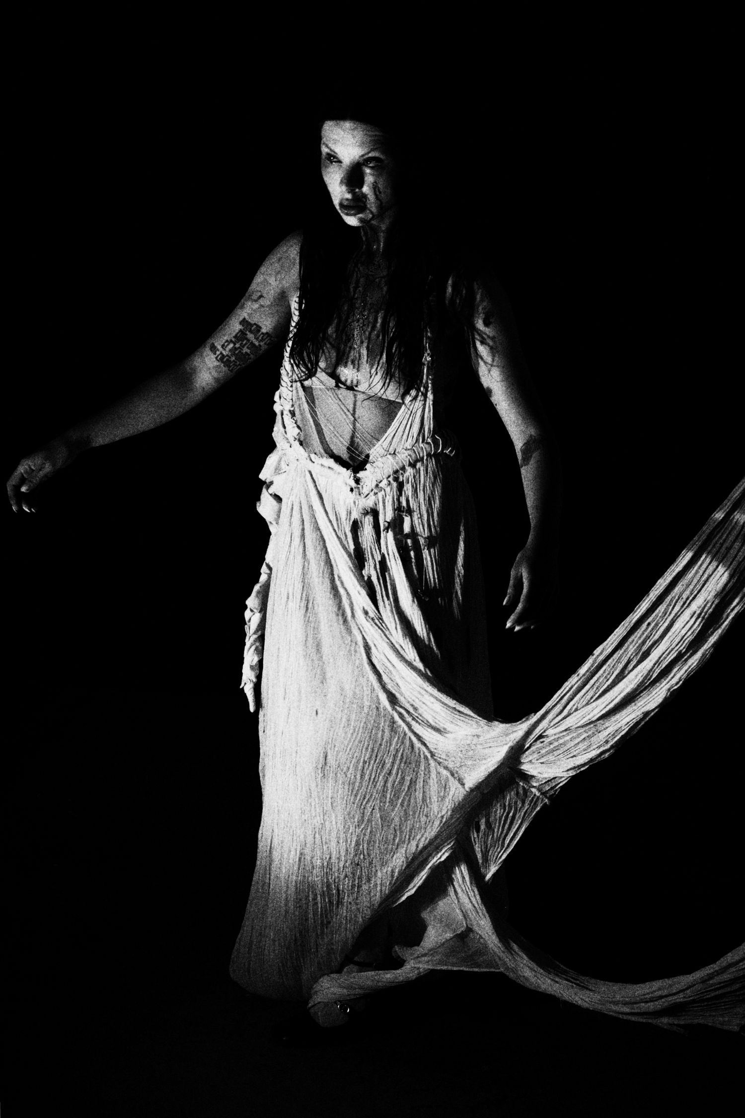 Black and white photo of a woman in a flowing white dress with long dark hair in dramatic dark lighting.