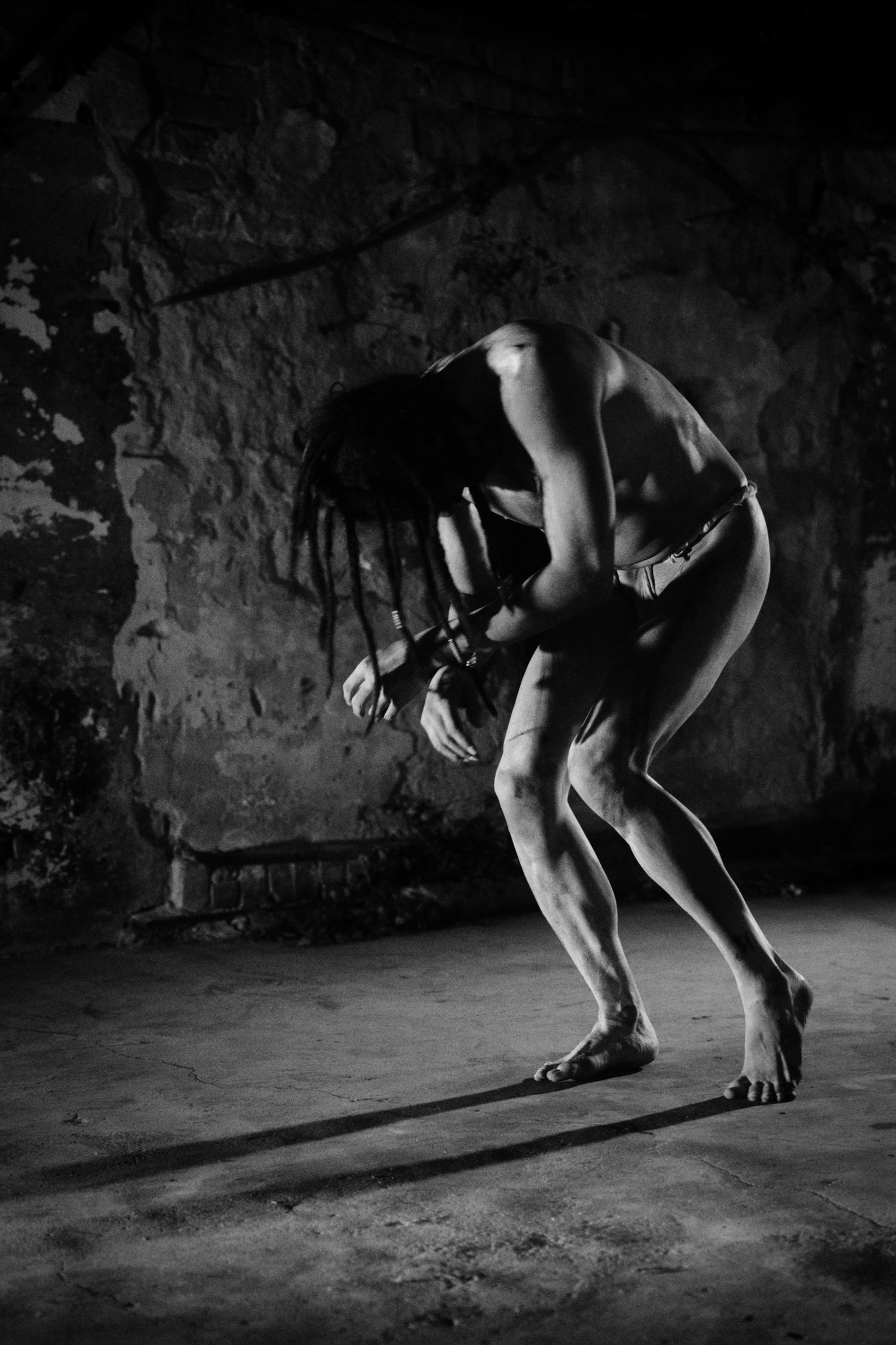 Black and white photo of a person in a dramatic bent pose in an abandoned stone room.