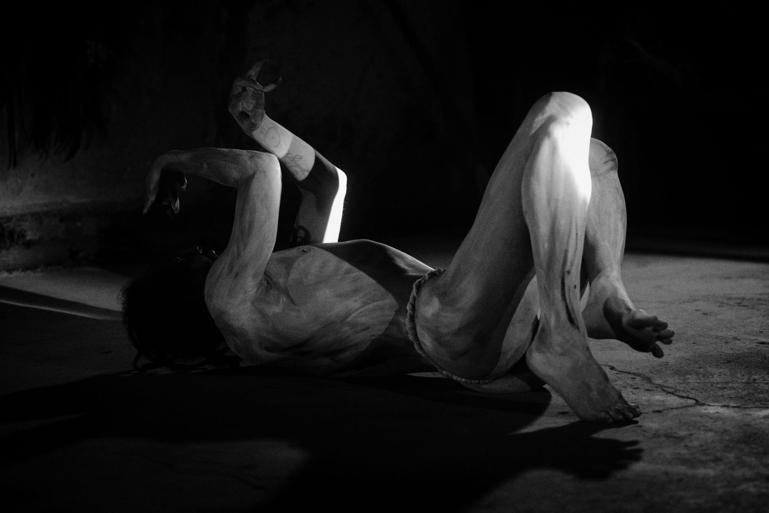 Black and white artistic photo of a figure reclining dramatically on a dark floor in expressive pose.
