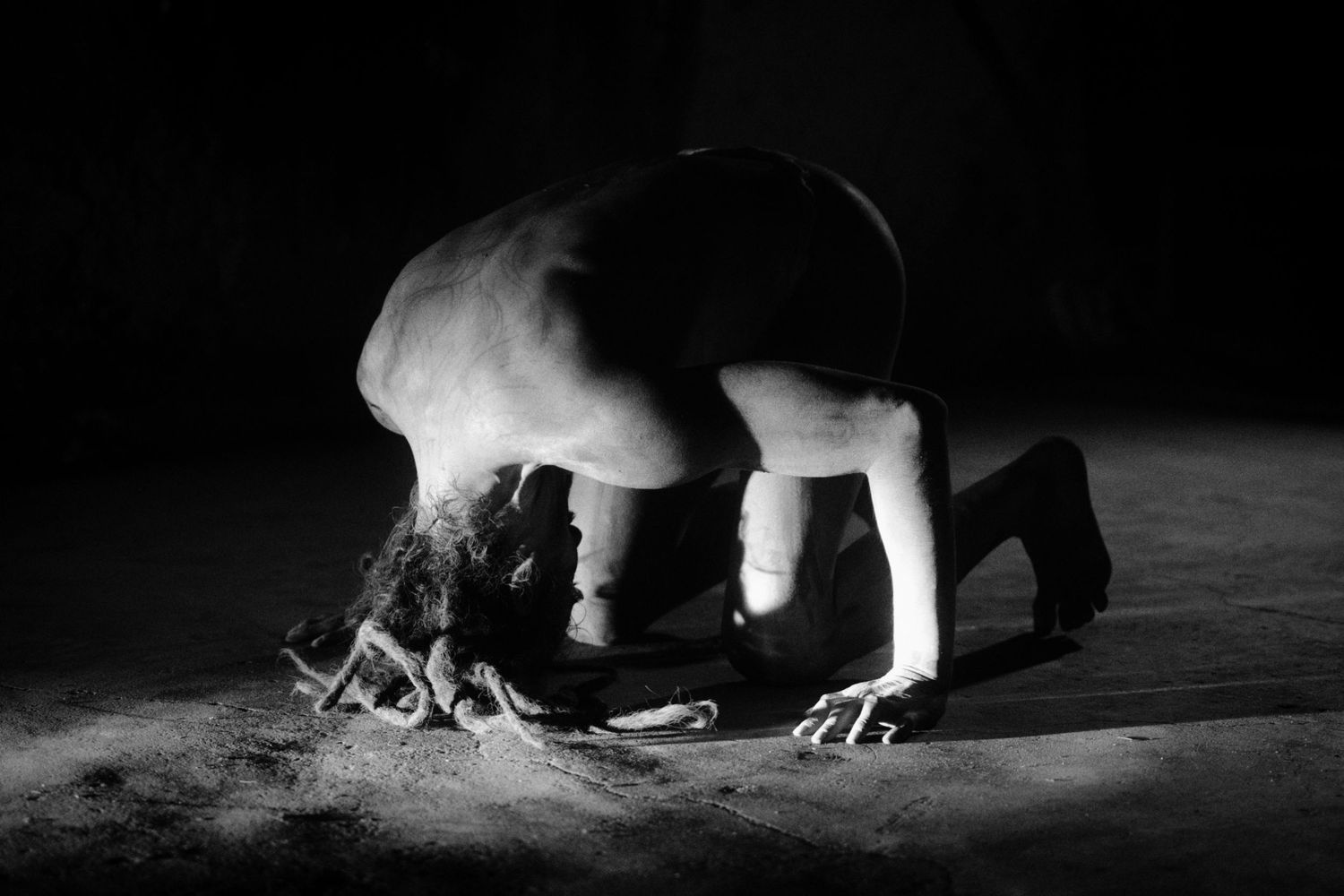 Black and white photo of a person crouching over bones on a dark floor with dramatic lighting.