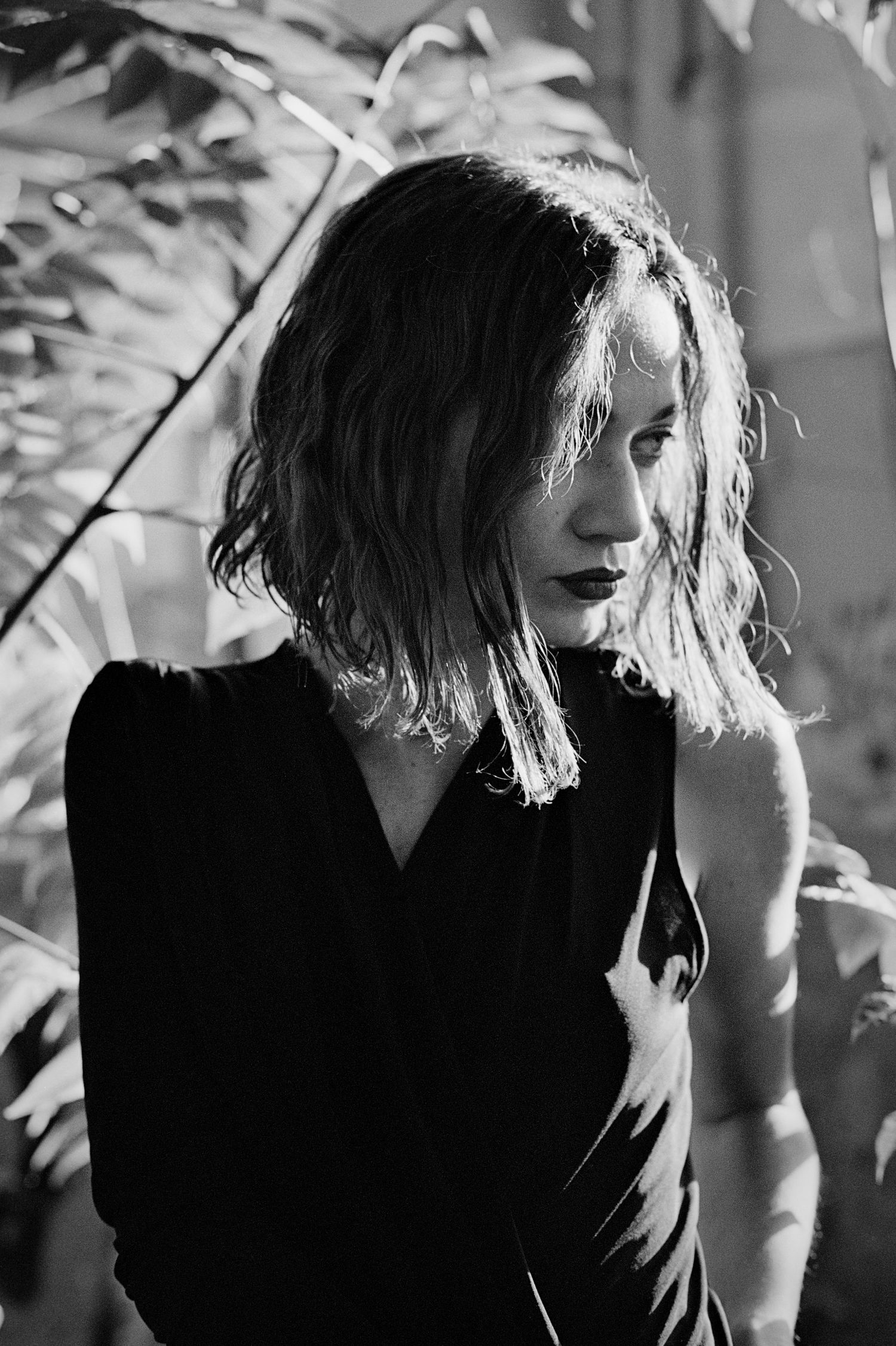 Black and white portrait of a woman with wavy bob hair in a black dress, surrounded by tropical leaves.