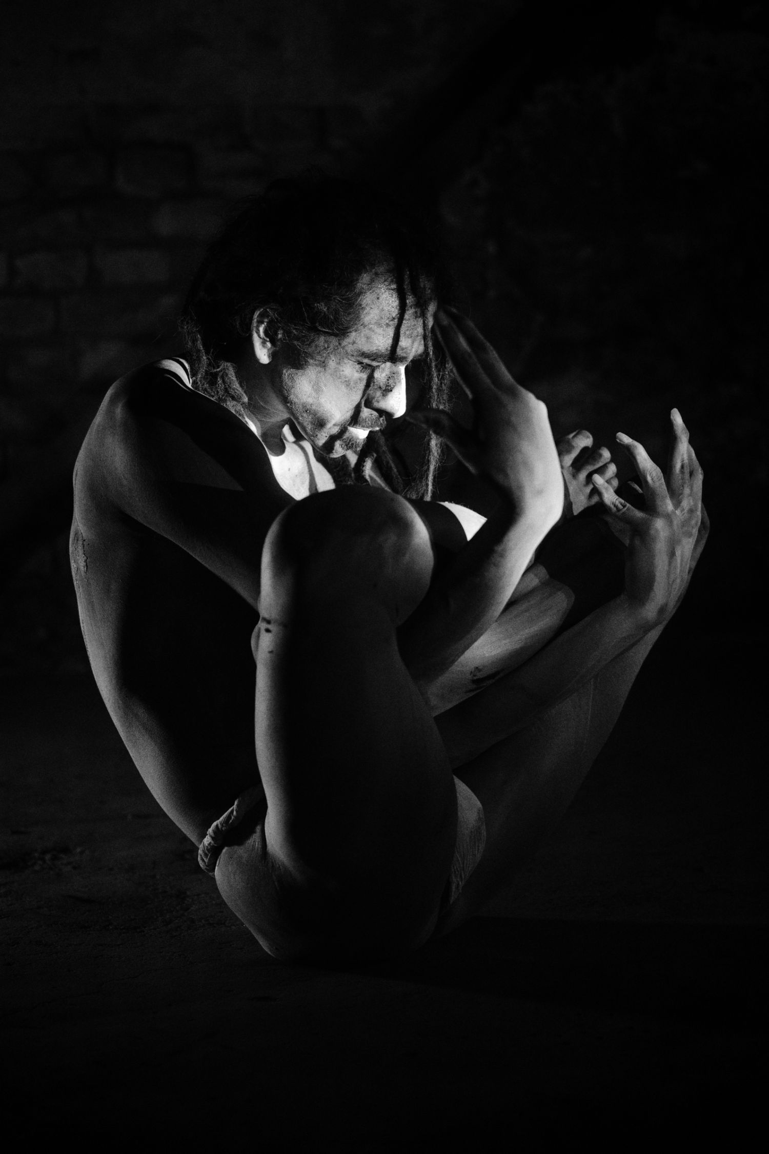 Black and white photo of a flexible dancer in a dramatic pose against a dark brick wall background.