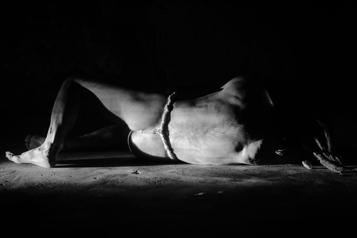 Black and white fine art photo of a figure lying on the ground in dramatic low-key lighting.