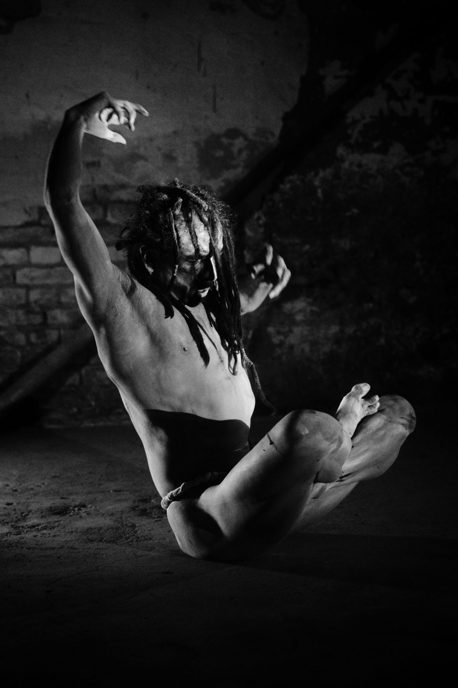 Black and white photo of a muscular dancer with dreadlocks in an expressive pose on the floor.