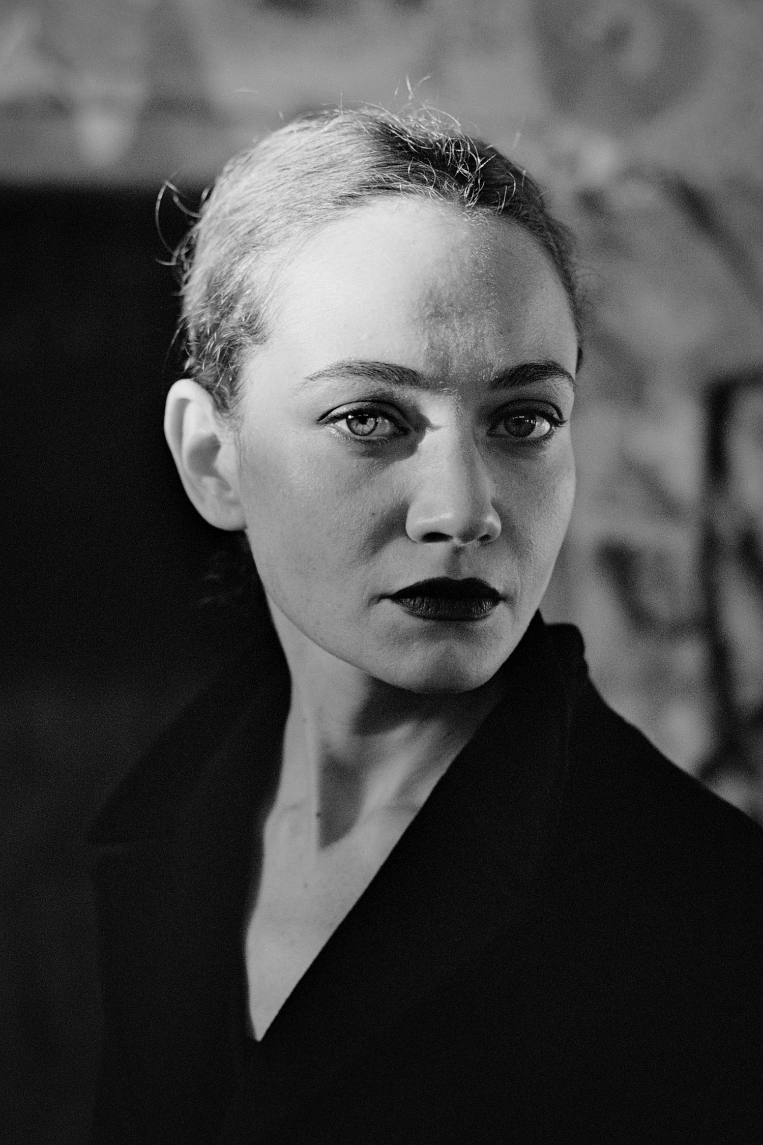 Black and white portrait of a woman with slicked-back hair and dark lipstick wearing a black jacket.