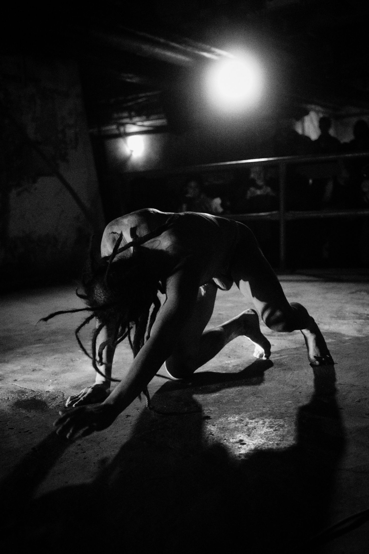 Black and white photo of a dancer crouching dramatically on stage under a bright spotlight in a dark venue.