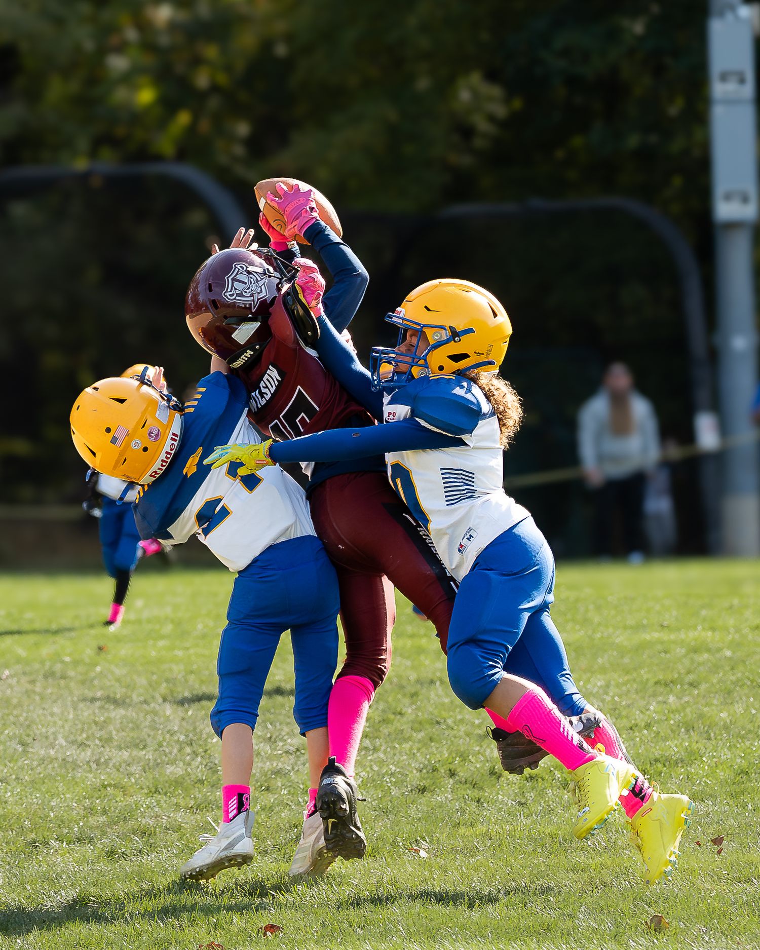 Football player jumping up to make a catch with two opposing teammates on either side of him.