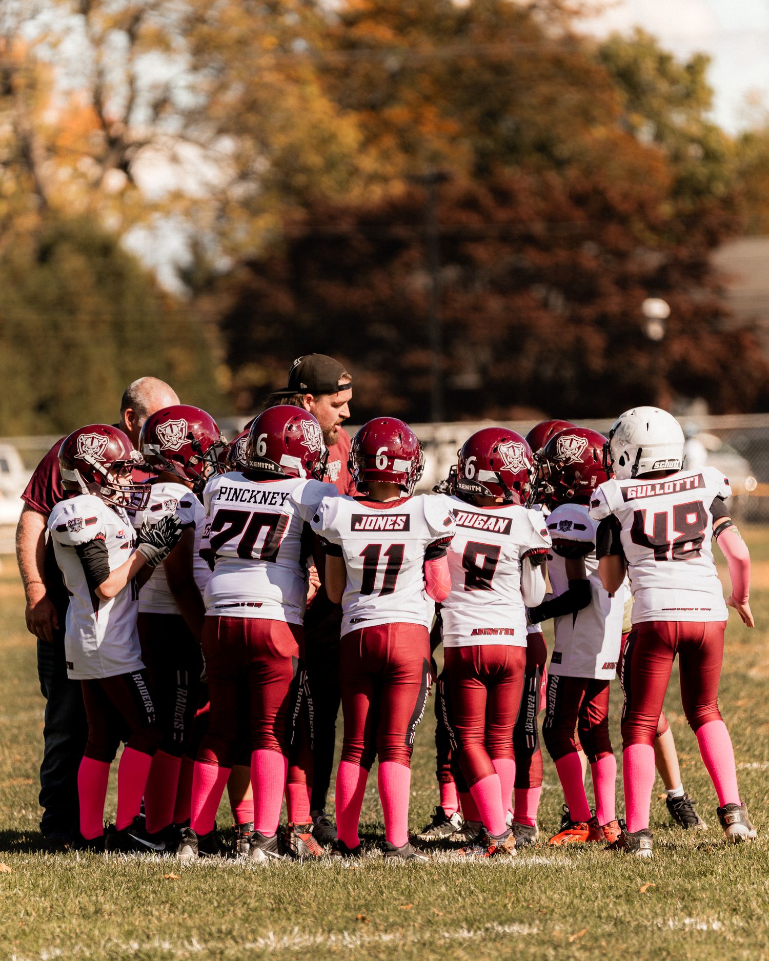 Image of young football team athletes with their backs turned listening to the coach in a huddle.