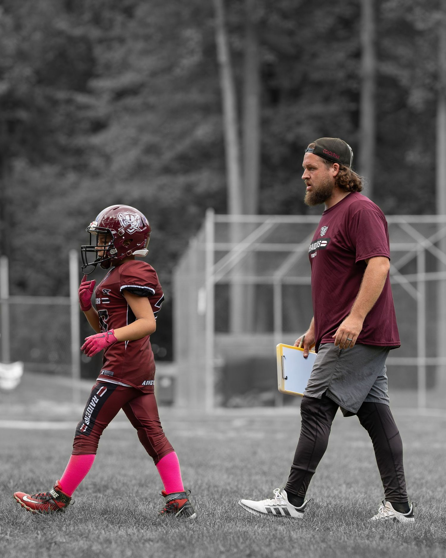 Football player walking off camera with football coach dad behind him.