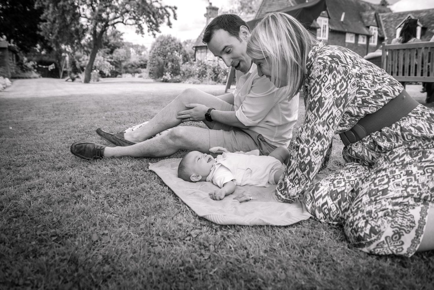 Parents tenderly caring for newborn baby on a blanket in a garden.