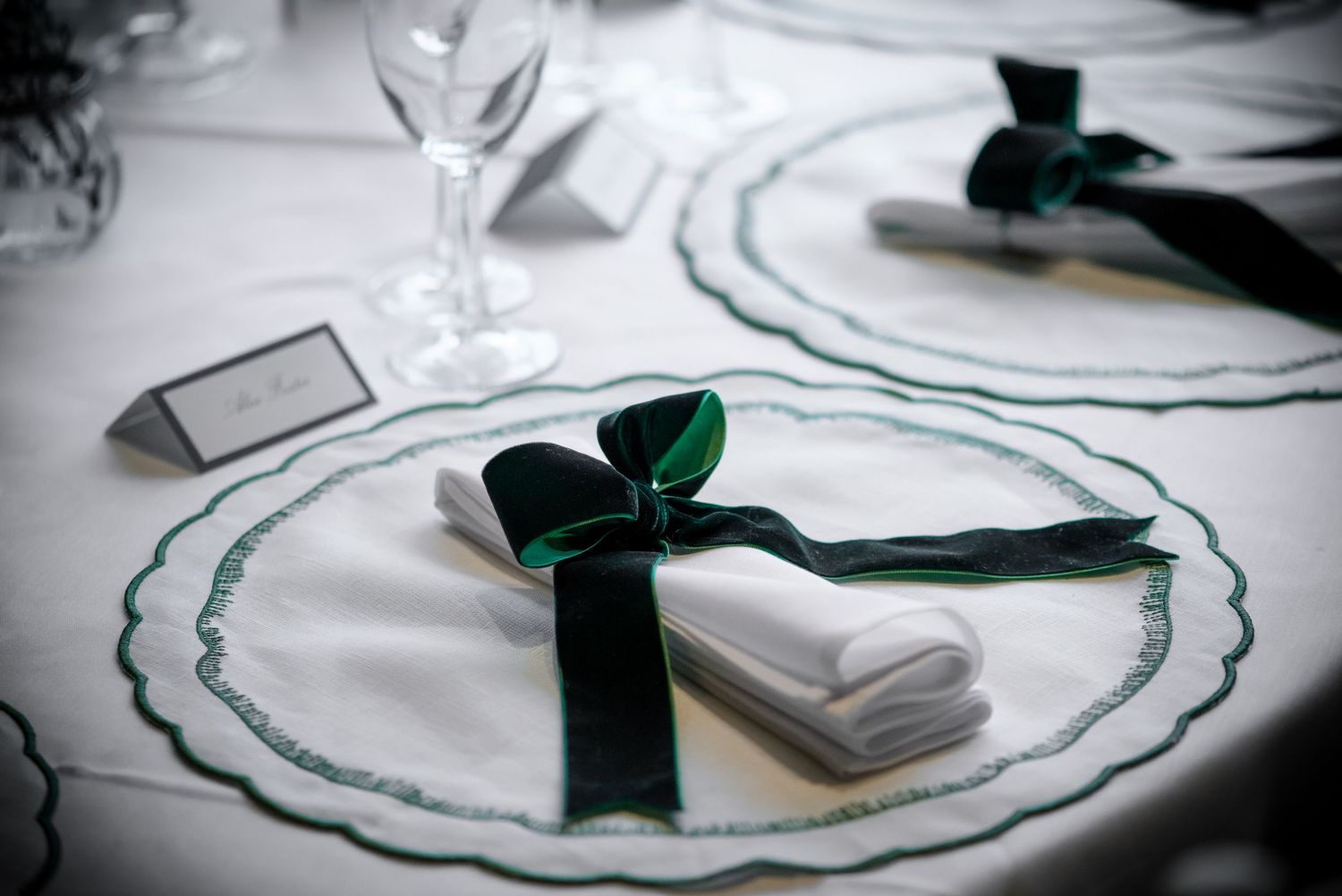 Close-up of elegant wedding place setting with green embroidered plate and dark green velvet ribbon bow napkin.