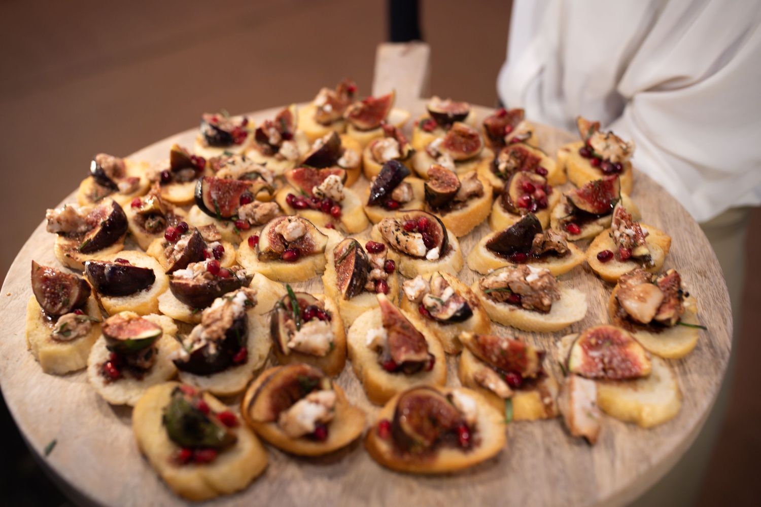 Assorted fig and cheese canapes arranged on a round wooden serving board.
