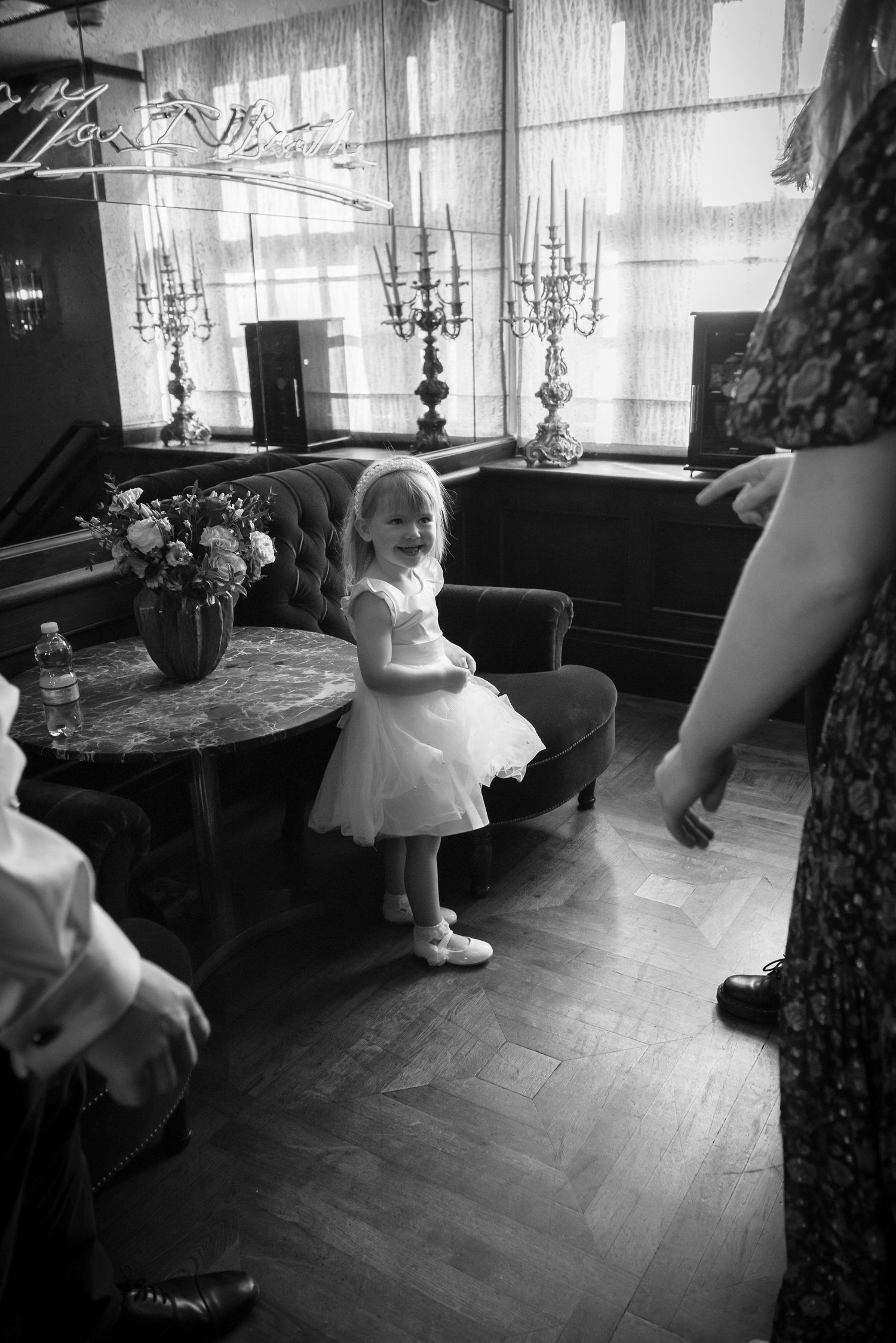 Young flower girl in white tutu dress smiling joyfully at an elegant wedding venue interior.