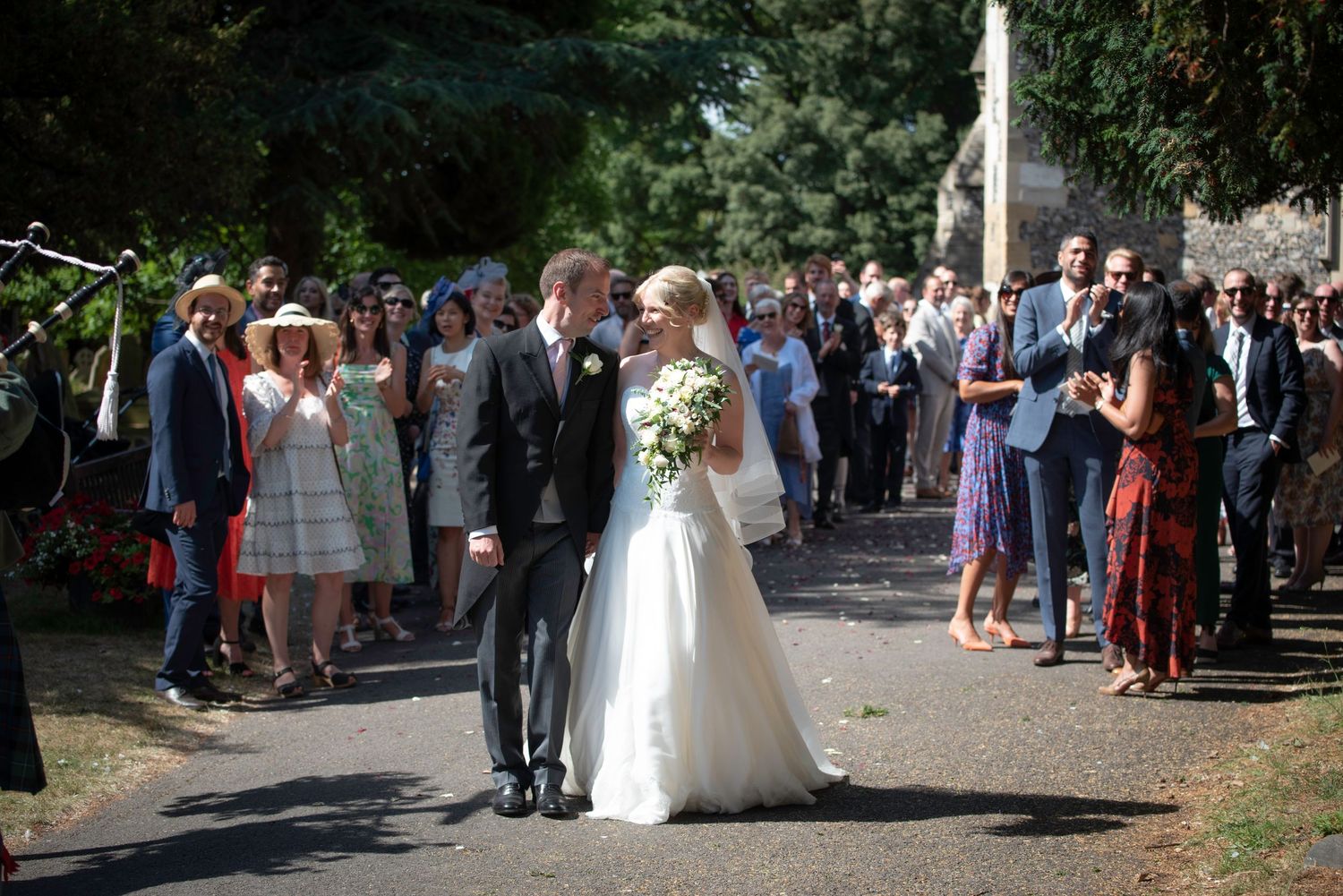 Newlywed couple kissing outside church surrounded by cheering wedding guests on sunny day. St Michaels Church, Bray
