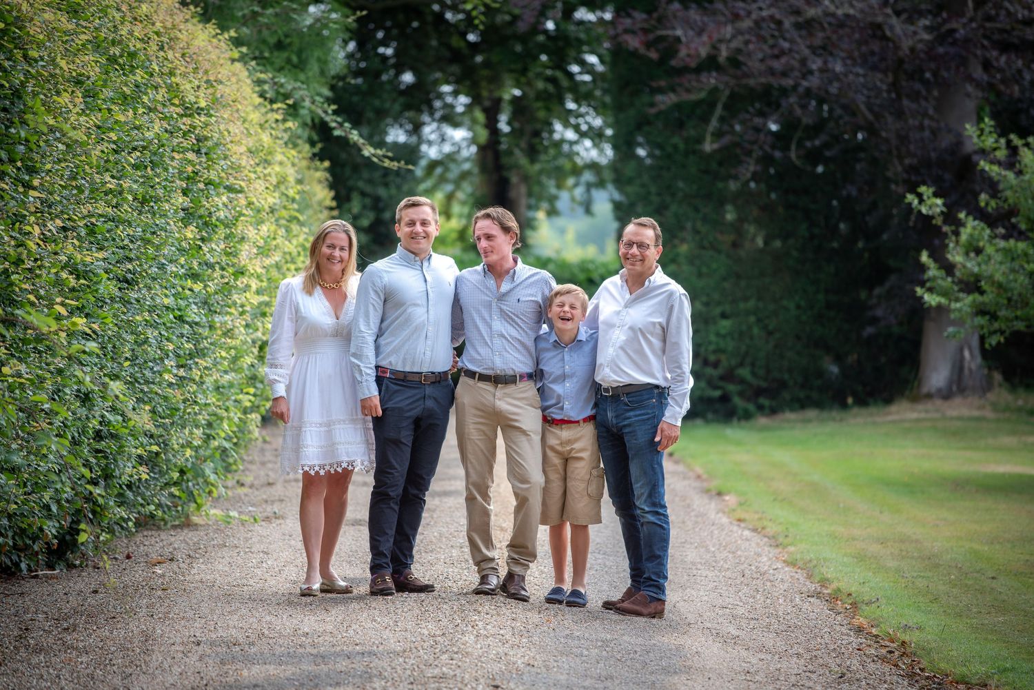 Cheerful family group smiling on a gravel pathway bordered by tall manicured hedges. family portrait