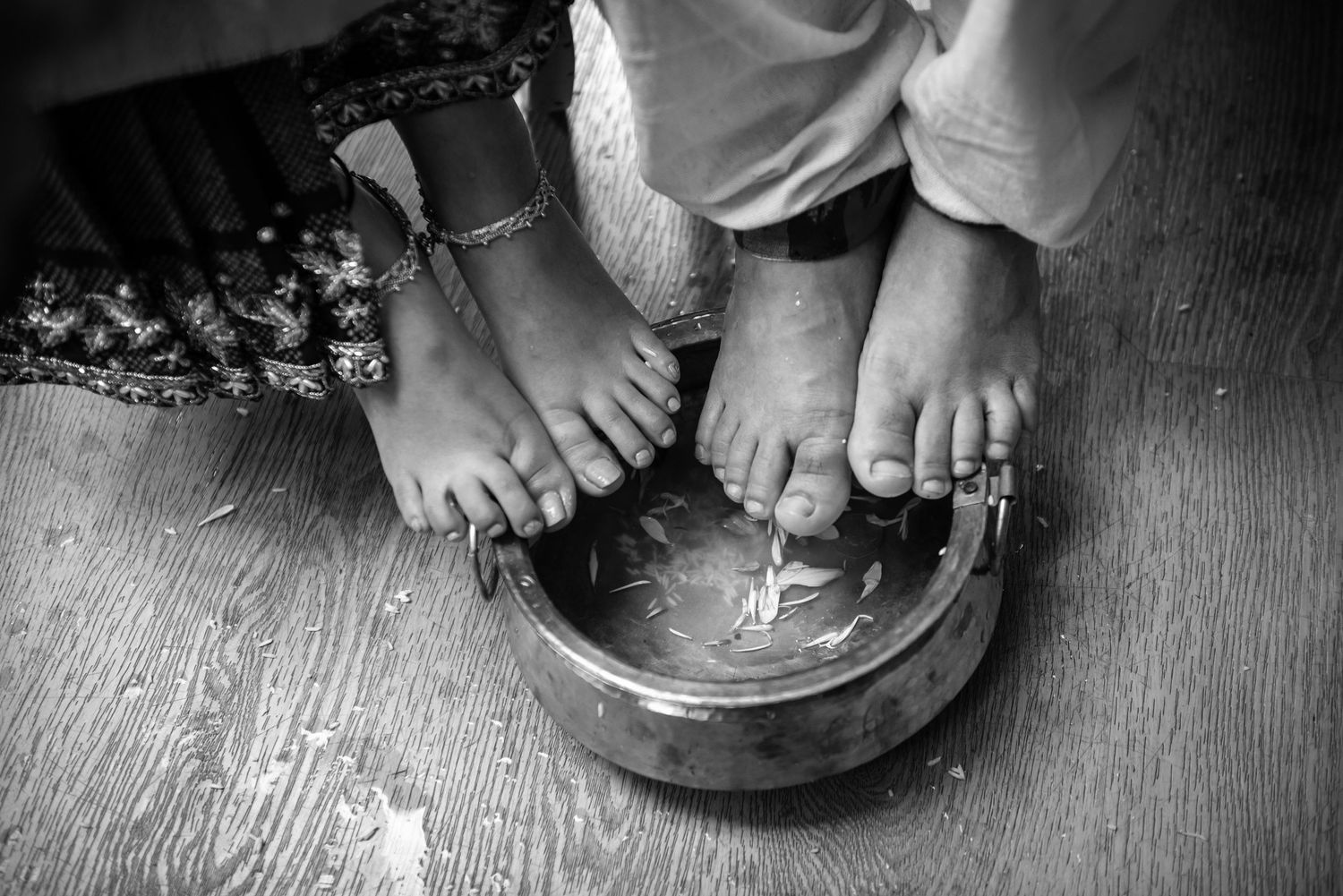 Black and white close-up of two pairs of feet in a ceremonial bowl during traditional wedding ritual.