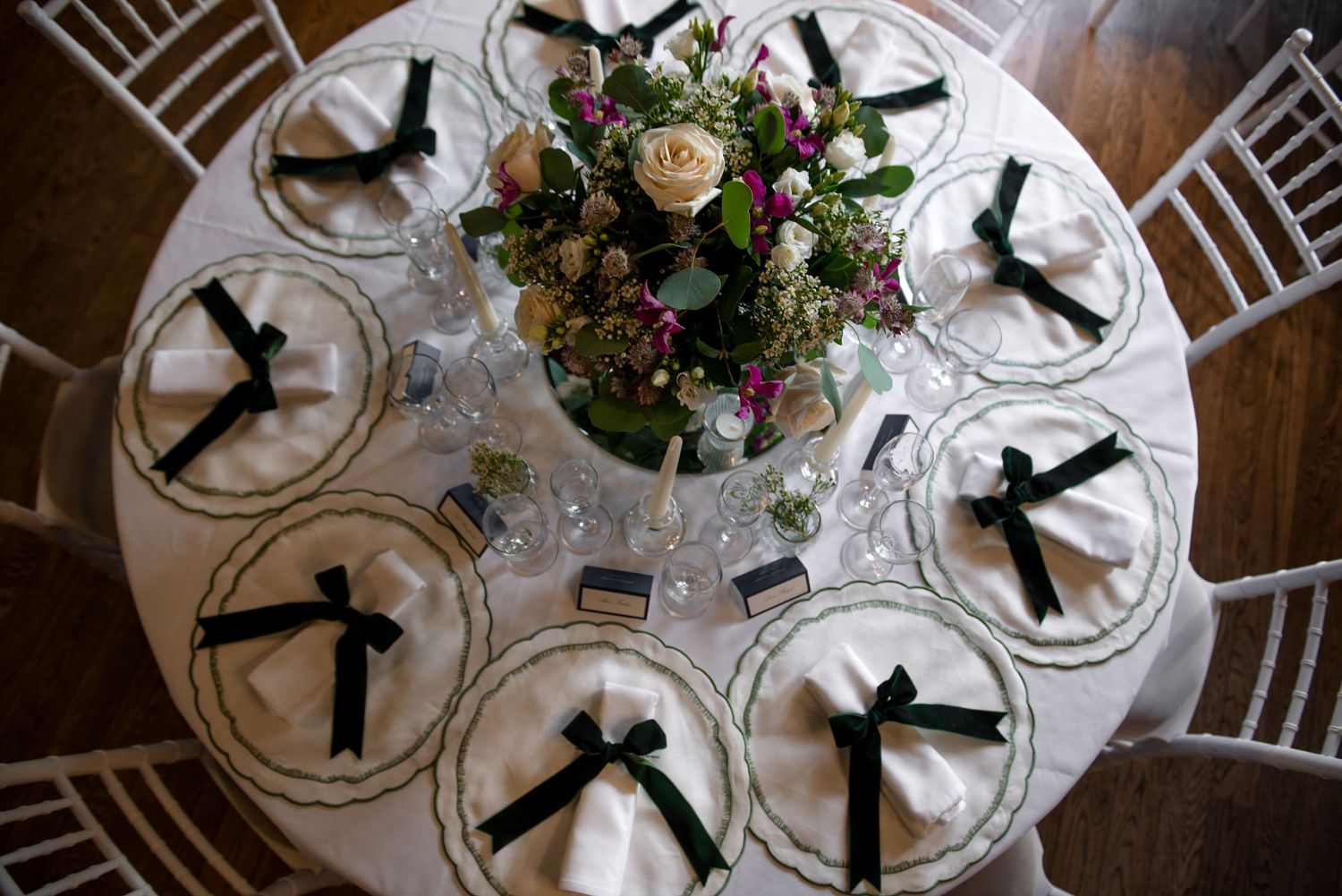 Overhead view of elegant round wedding table with green-bordered plates, black ribbon napkins, and floral centerpiece.