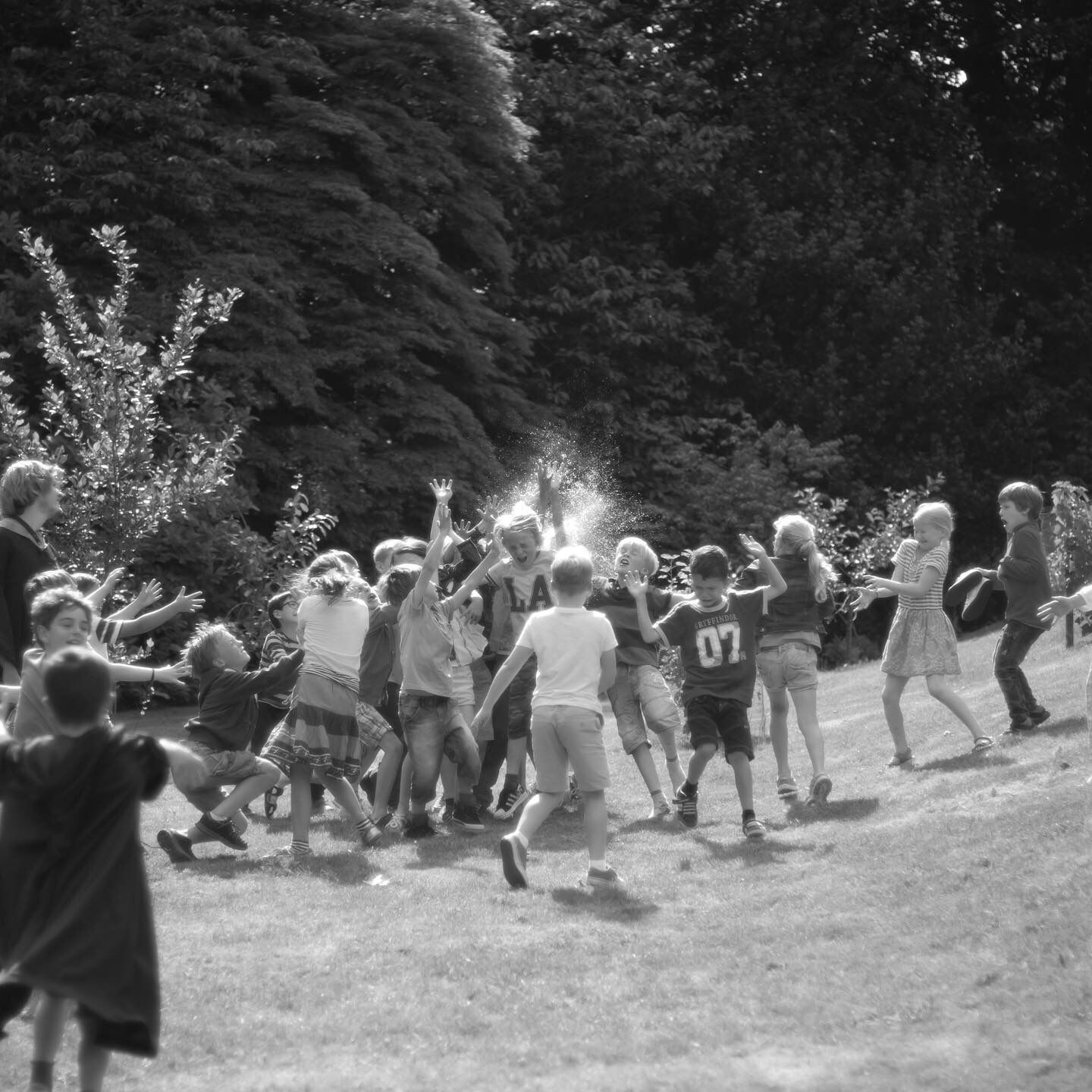 Black and white photo of children playing outdoors in a sunny garden surrounded by trees.