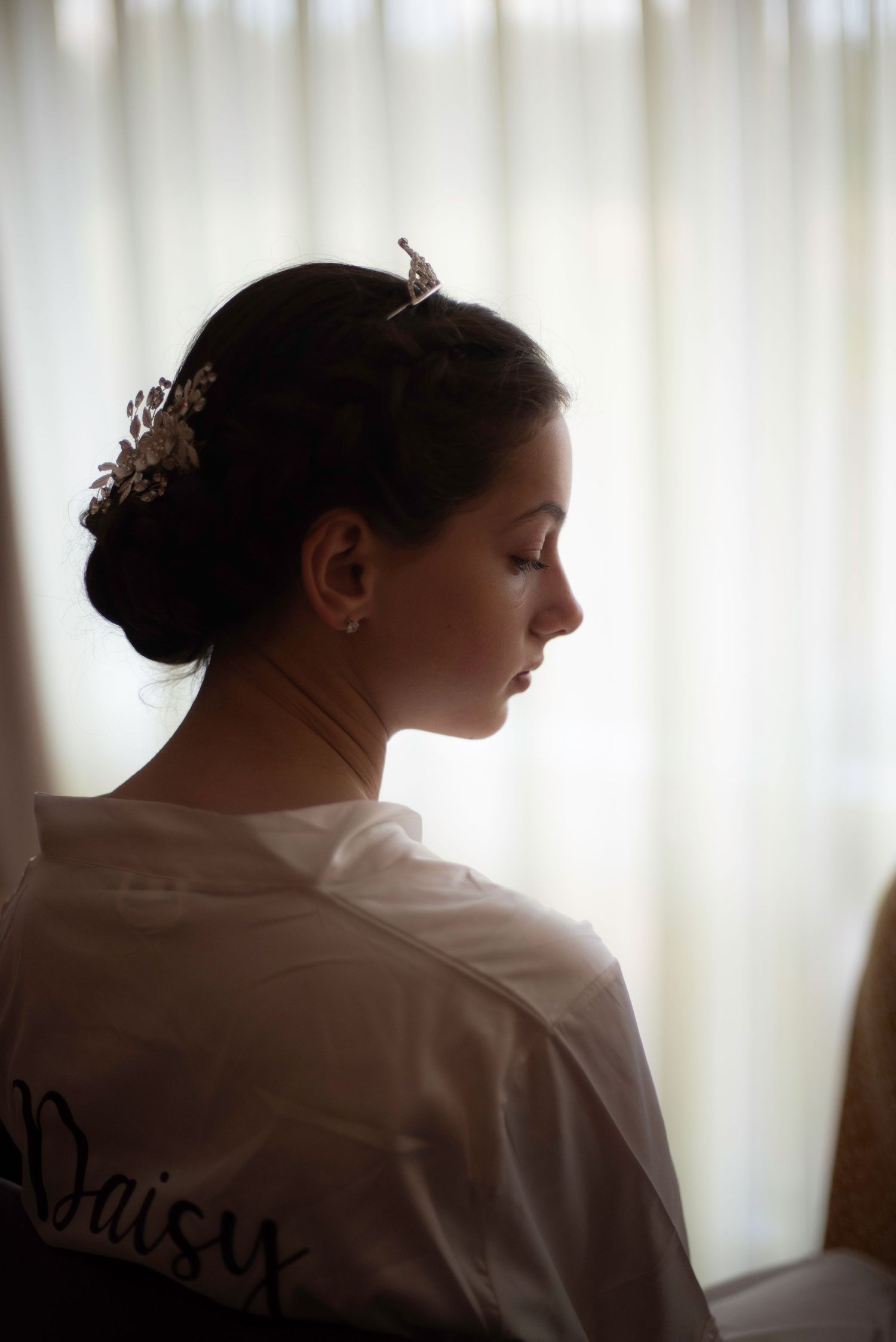 Elegant bridesmaid with updo hairstyle and floral hair accessory wearing personalized satin robe.