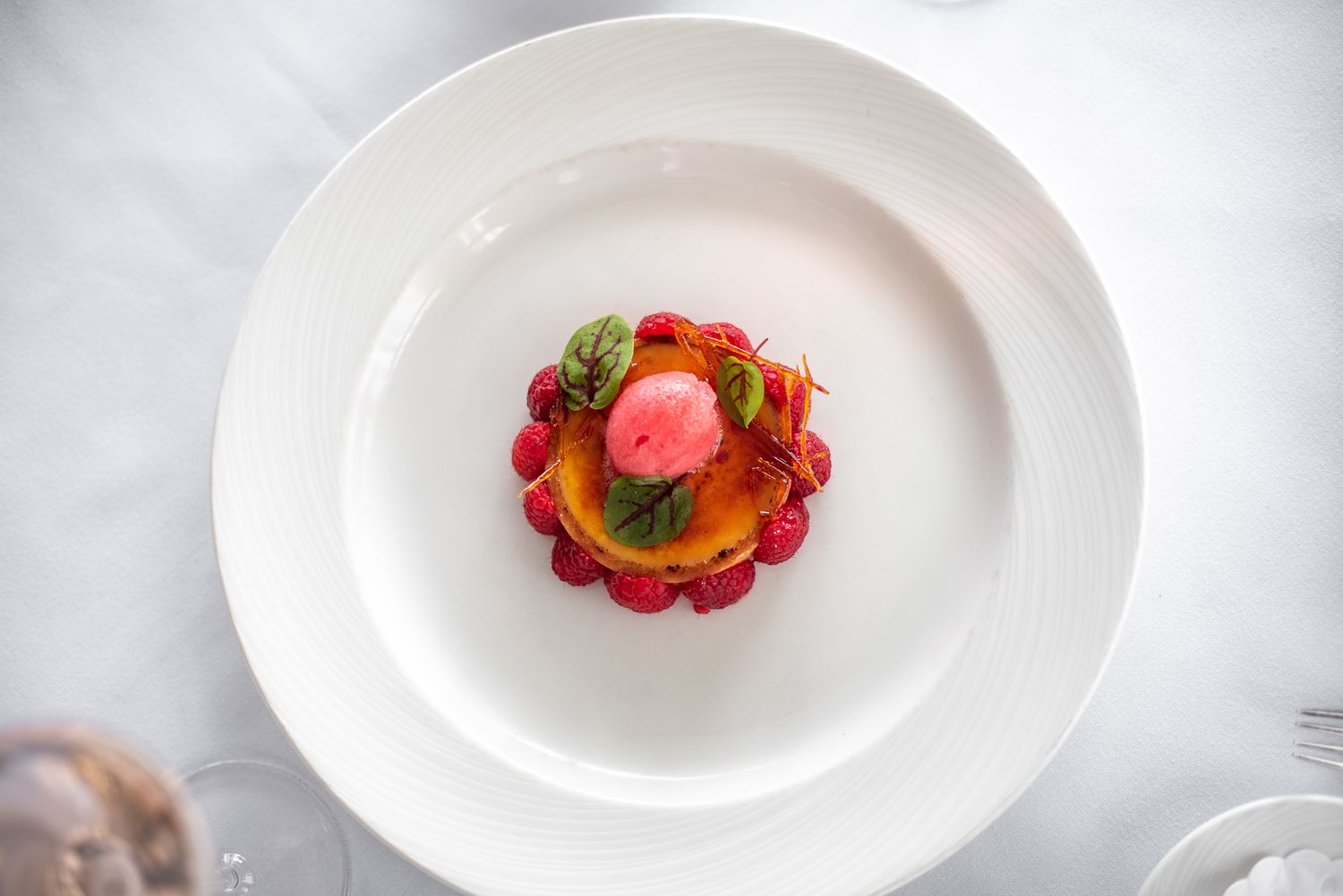 Elegant dessert with pink sorbet, raspberries, and mango on a white plate, fine dining style.