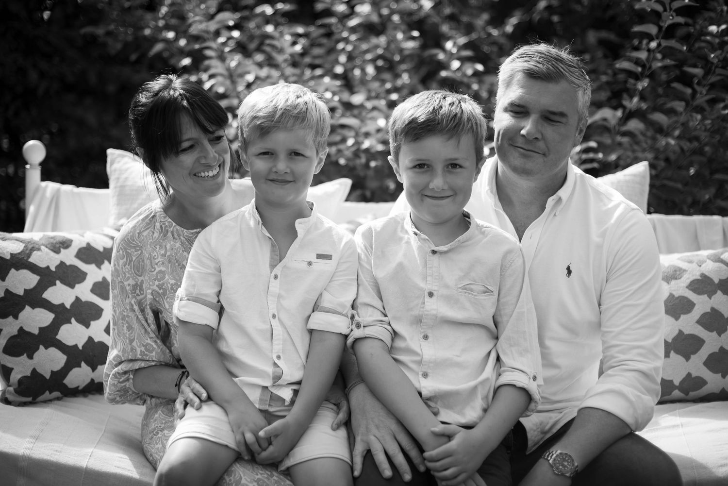 Black and white family portrait of parents with two boys seated on an outdoor bench. family portrait