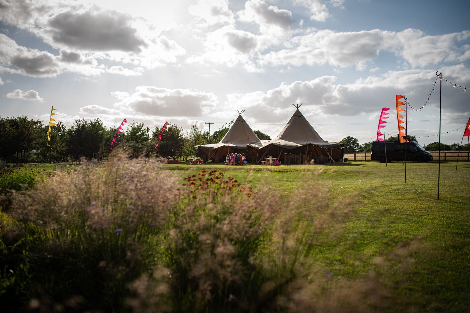 Rustic tipi wedding venue with colorful flags set among wildflowers under a dramatic cloudy sky.