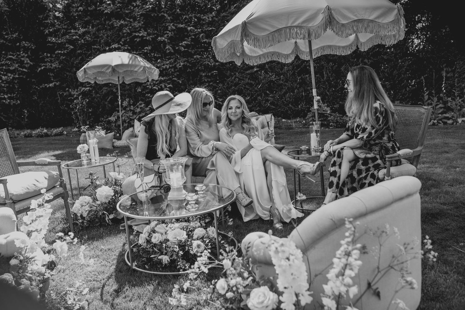Wedding guests relax outdoors under parasols surrounded by floral arrangements.