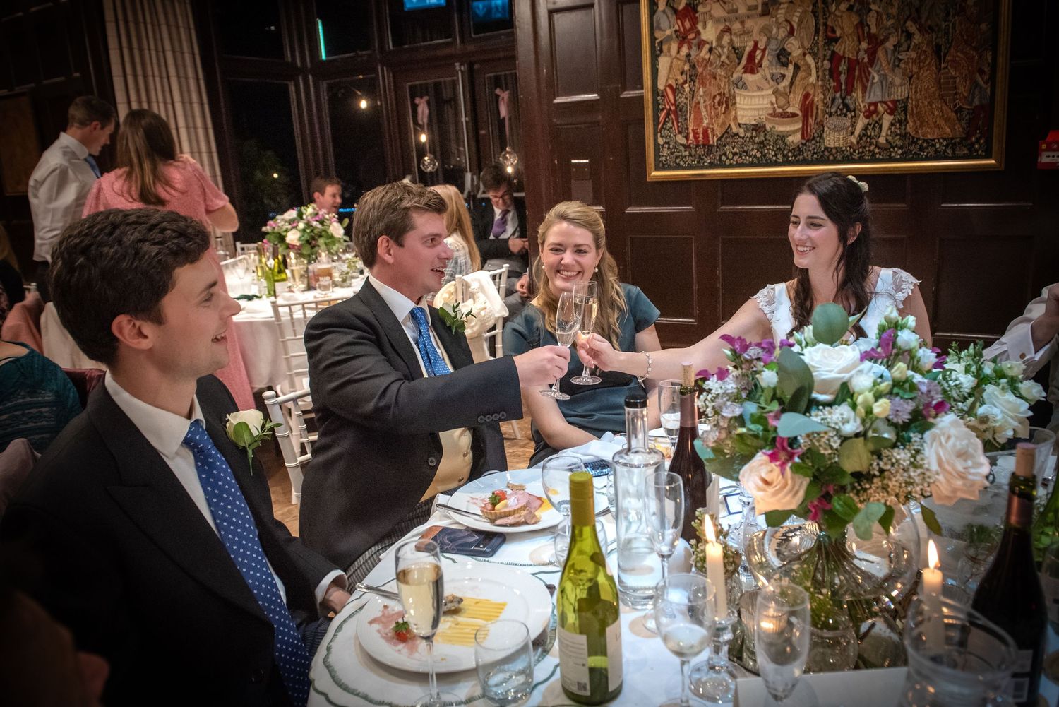 Bride clinking champagne glasses with a guest at a wedding reception in an elegant wood-paneled venue.