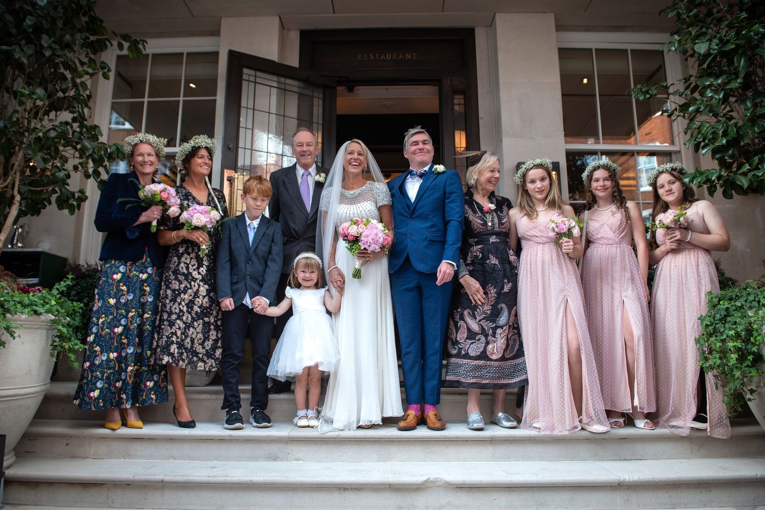 Bride and groom with wedding party posing on venue steps with bridesmaids in pink dresses.  London wedding.