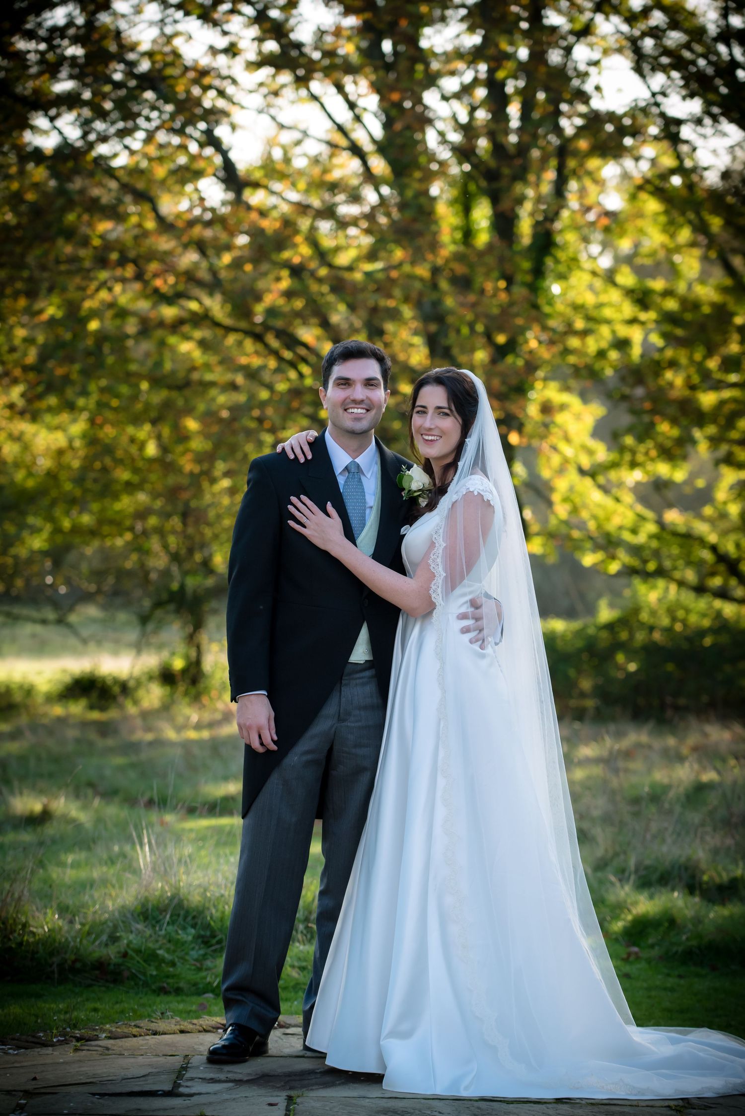 Bride and groom posing together in a sunlit autumn garden setting.