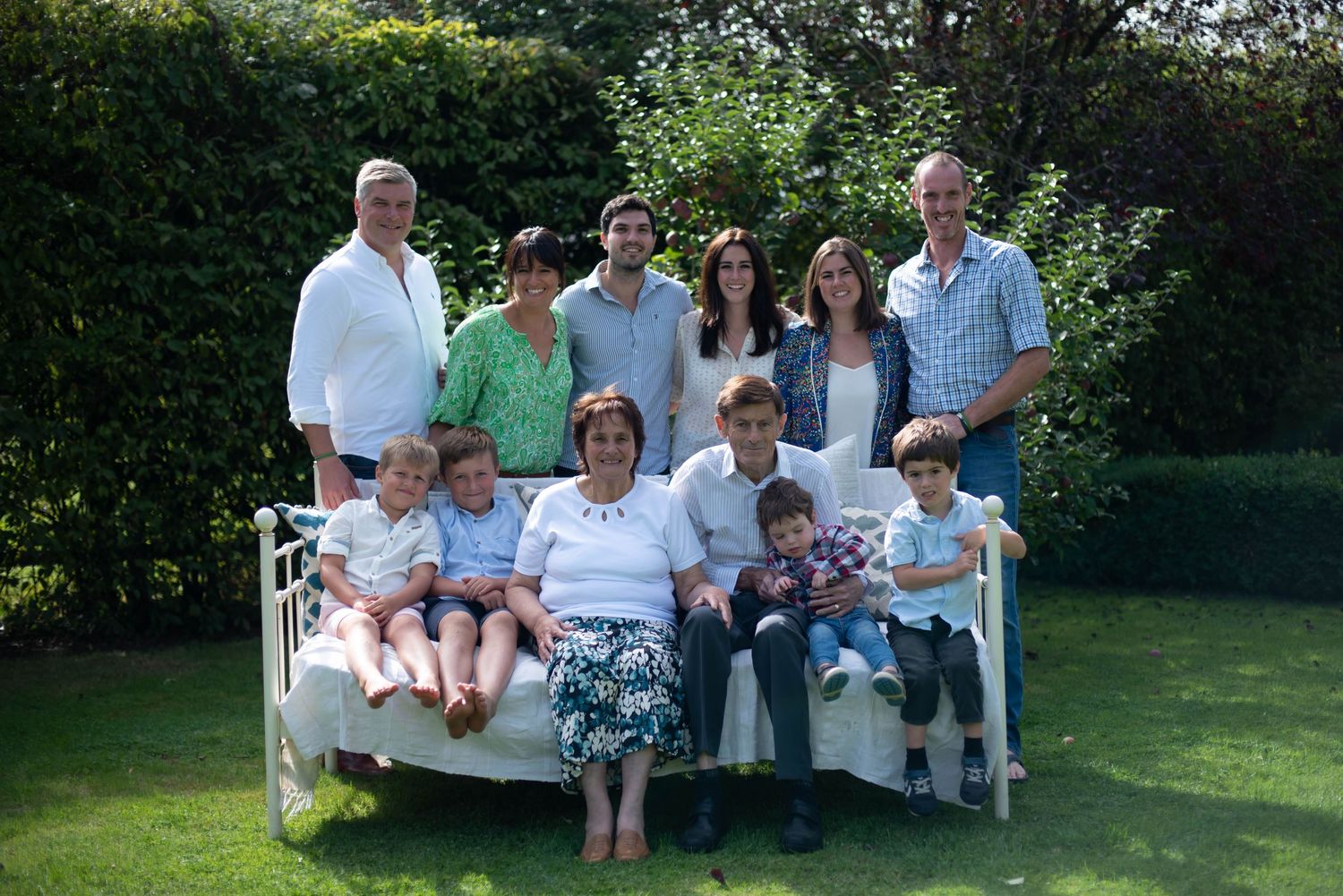 Large multigenerational family group portrait gathered together in a sunny garden.
