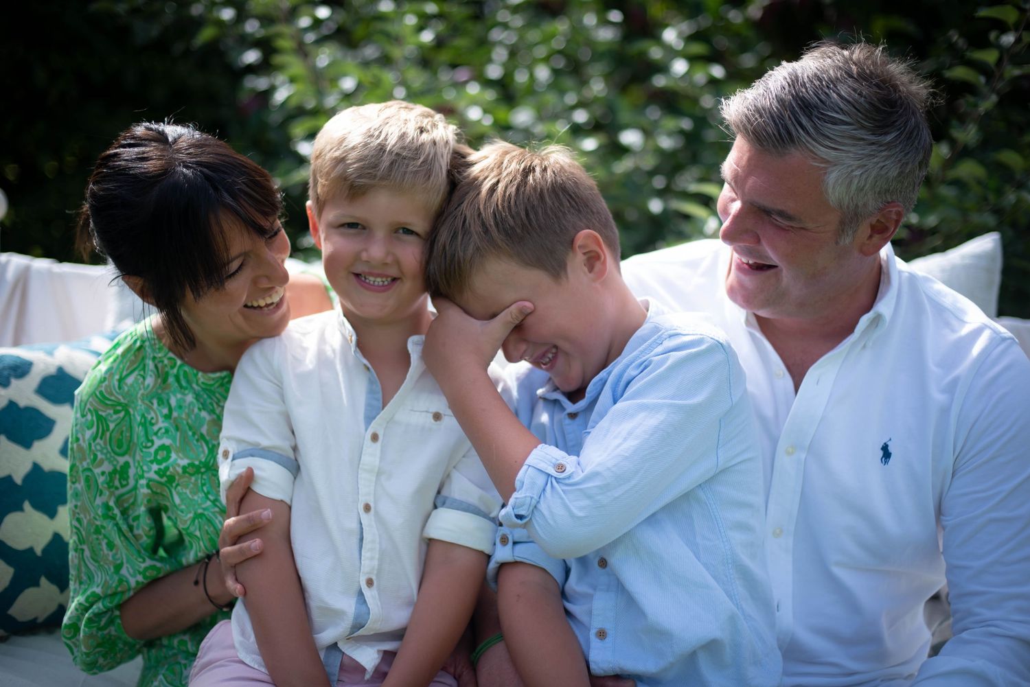 Joyful family of four sharing a candid laugh together on a garden bench outdoors.