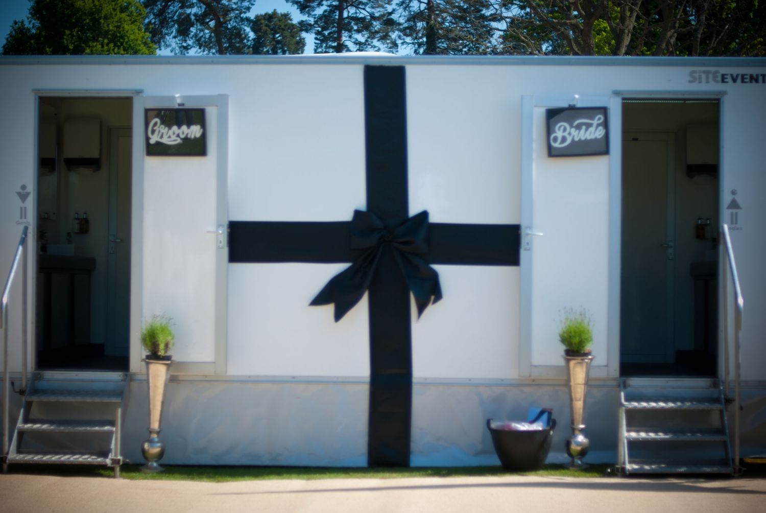 Elegant white wedding restroom trailer decorated with a large black bow for bride and groom.