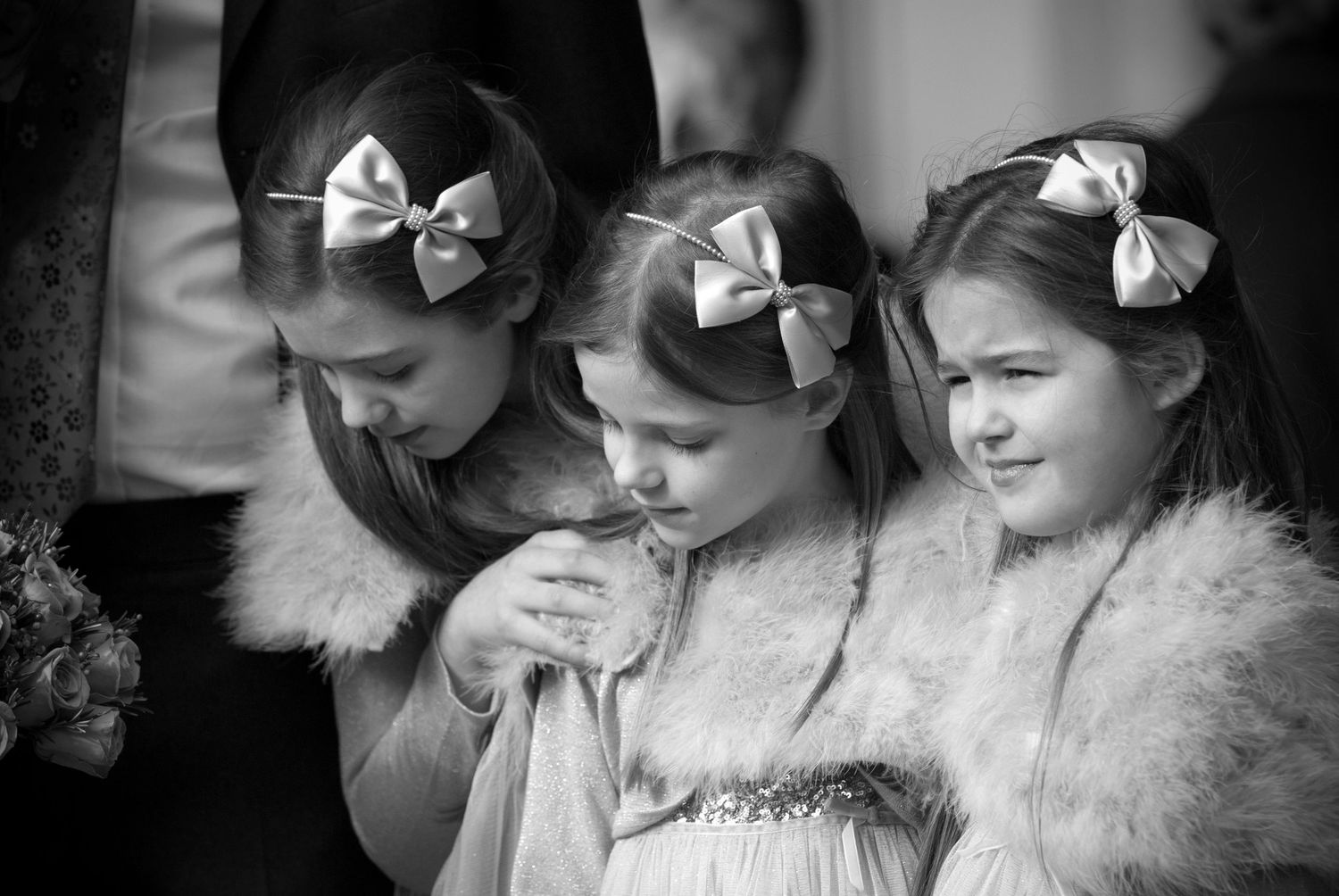 Three young flower girls with satin hair bows share a tender moment in black and white.  Windsor guildhall wedding
