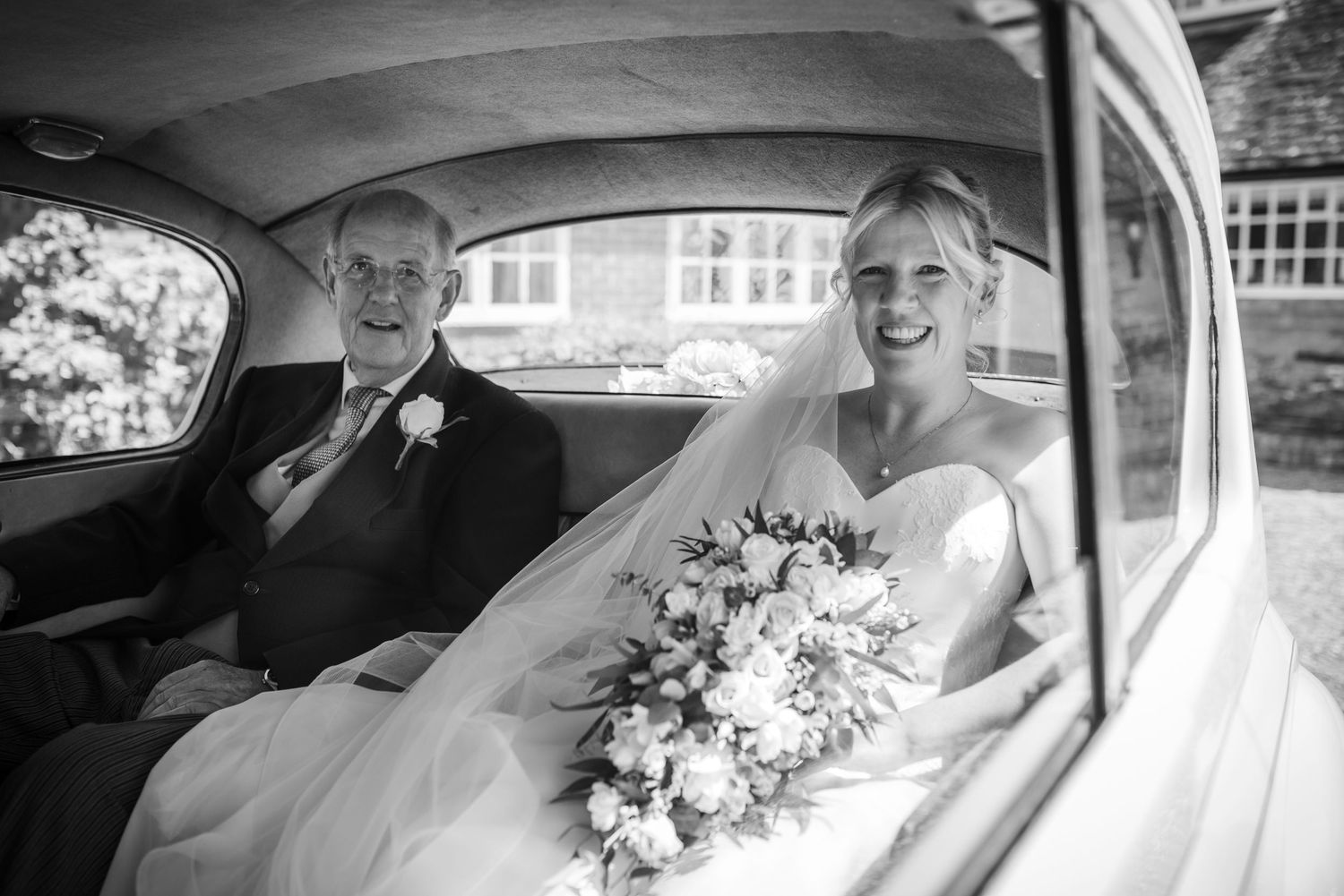 Black and white photo of smiling bride with bouquet seated in vintage wedding car.  St Michaels Church, Bray