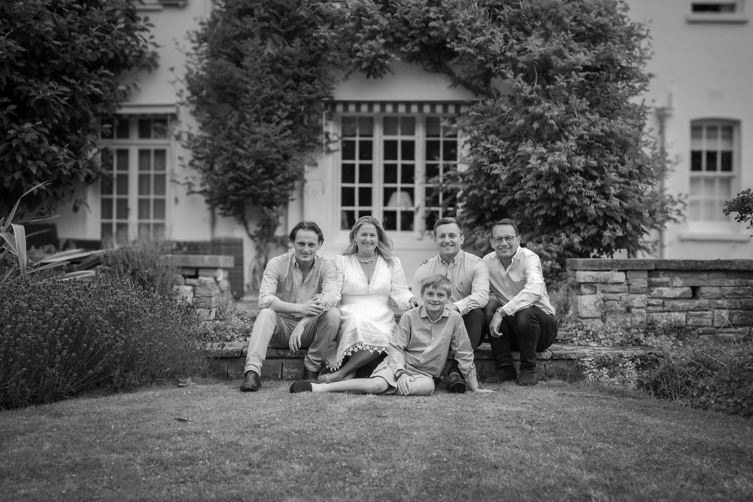Black and white family portrait of five people posing outdoors in front of a ivy-covered house.