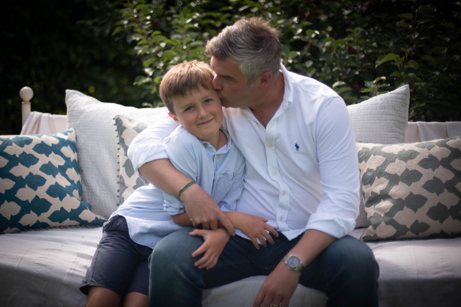 Father kissing young son on the cheek while sitting on an outdoor sofa.