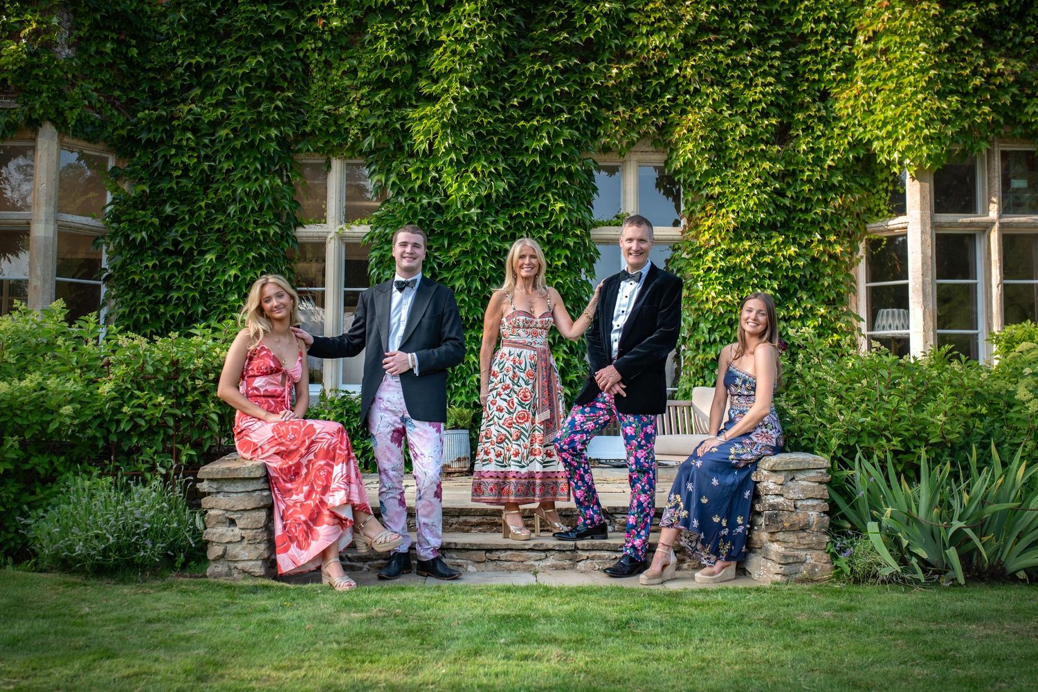 Five formally dressed people pose on stone steps in front of a grand ivy-covered building. family portrait