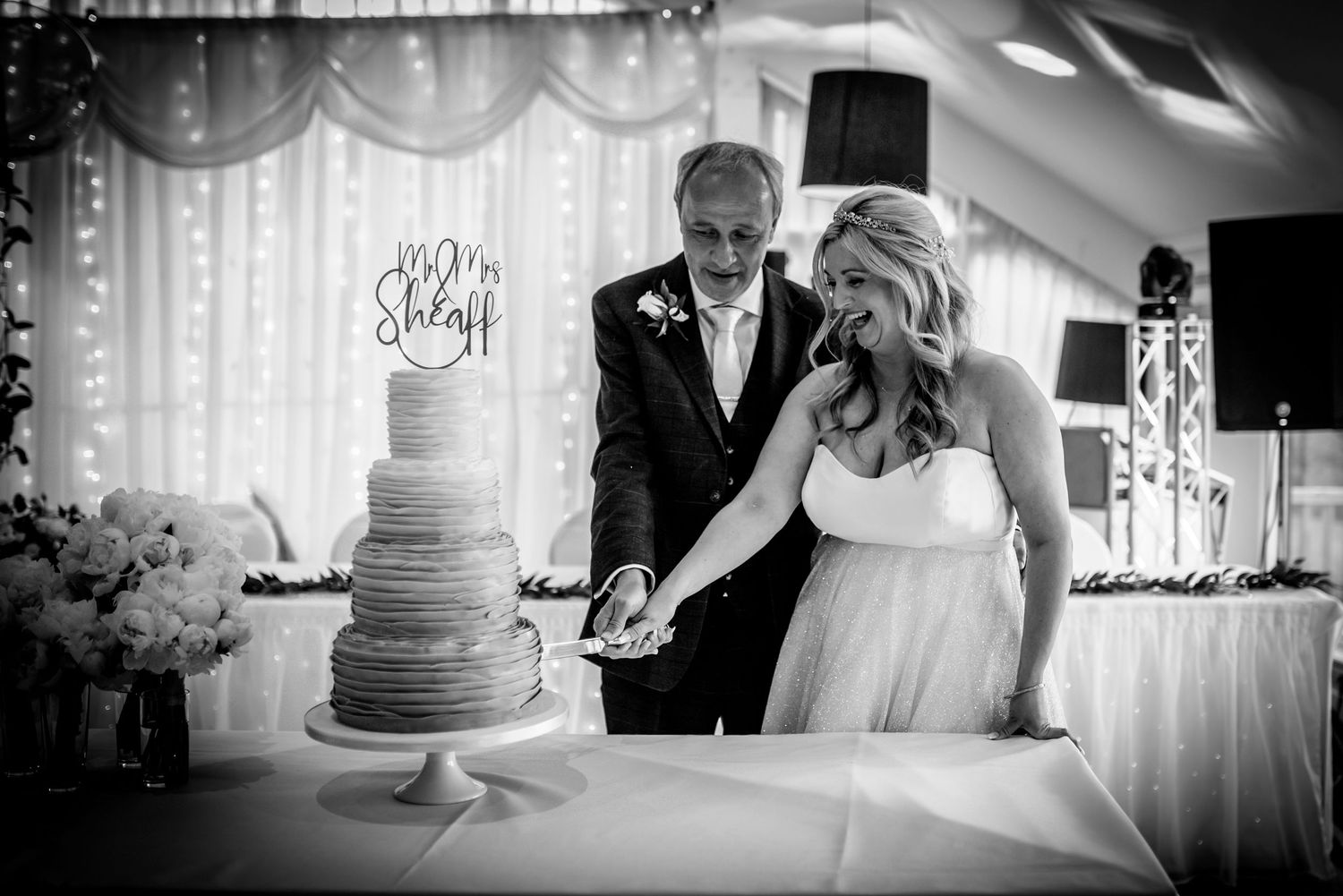 Bride and groom cutting their tiered wedding cake in elegant black and white photography.