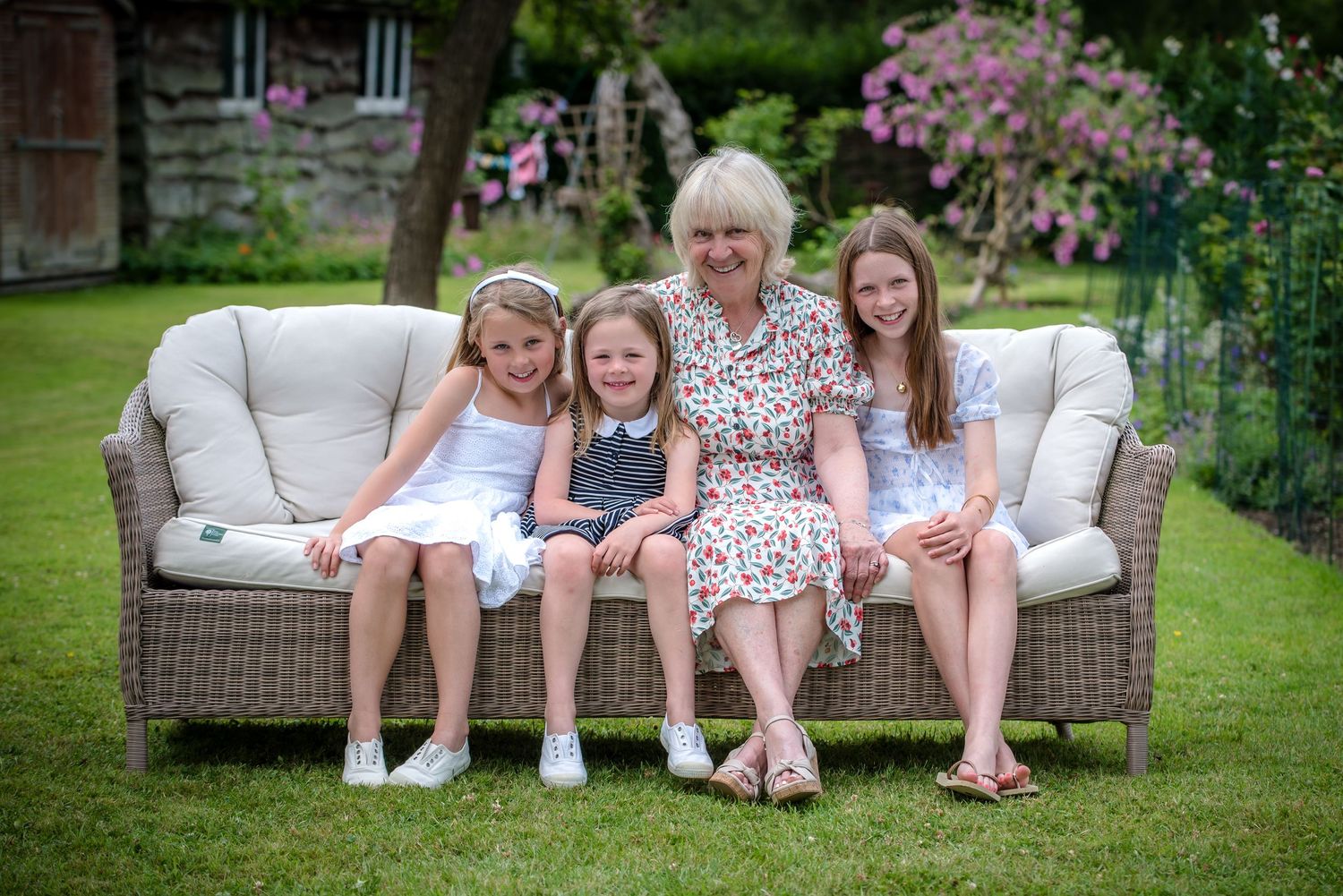Grandmother smiling with three granddaughters on a wicker sofa in a beautiful garden.