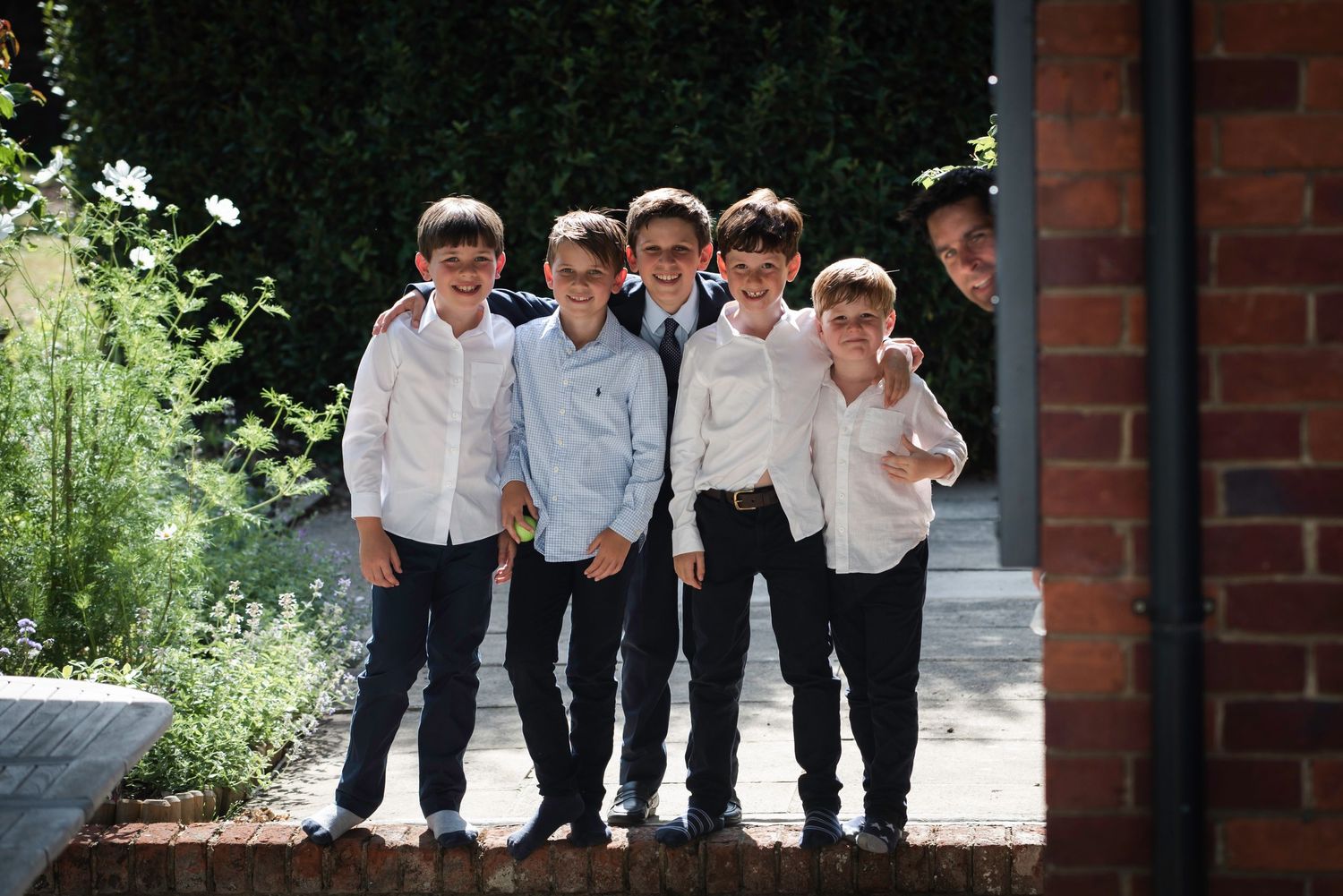 Color photo of six boys in white shirts laughing and posing together outside a brick building.
