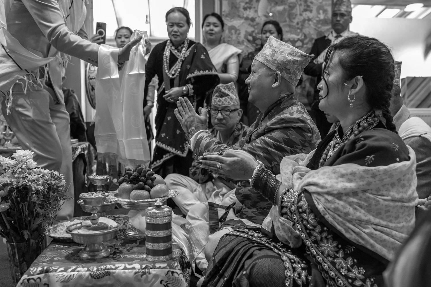 Black and white photo of a traditional Nepali wedding ceremony with guests in cultural attire performing rituals.