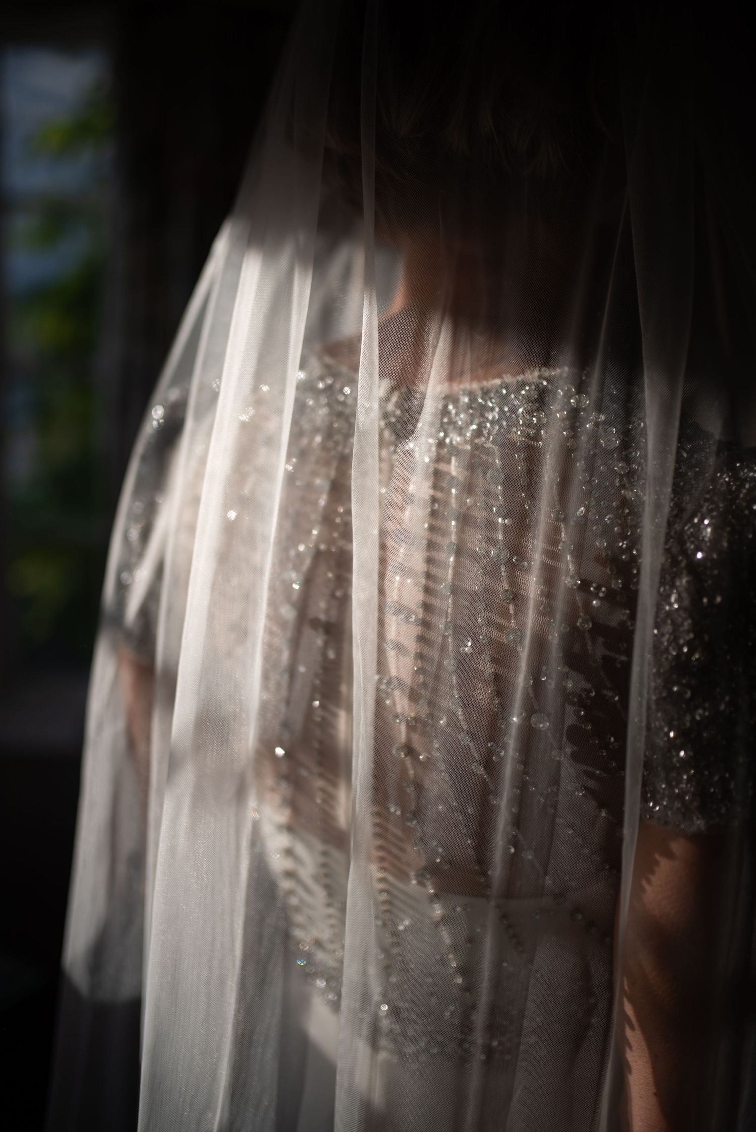 Ethereal color photo of bride in sparkly beaded wedding dress seen through flowing white veil.
