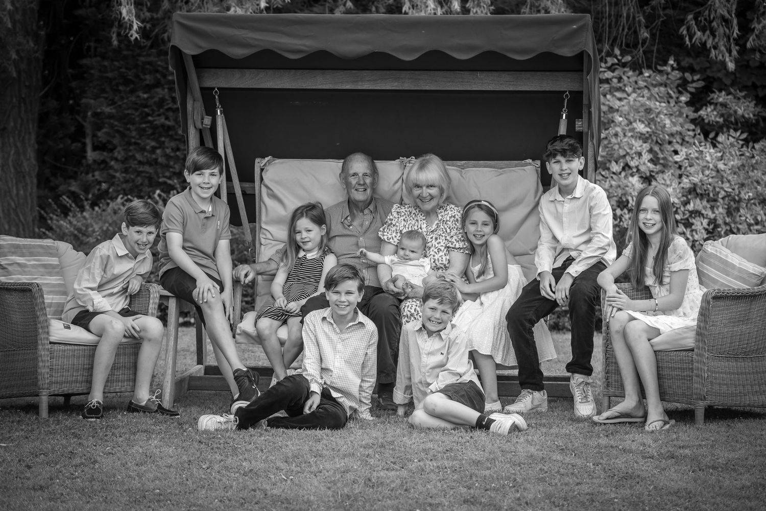 Black and white photo of grandparents surrounded by grandchildren in garden setting.
